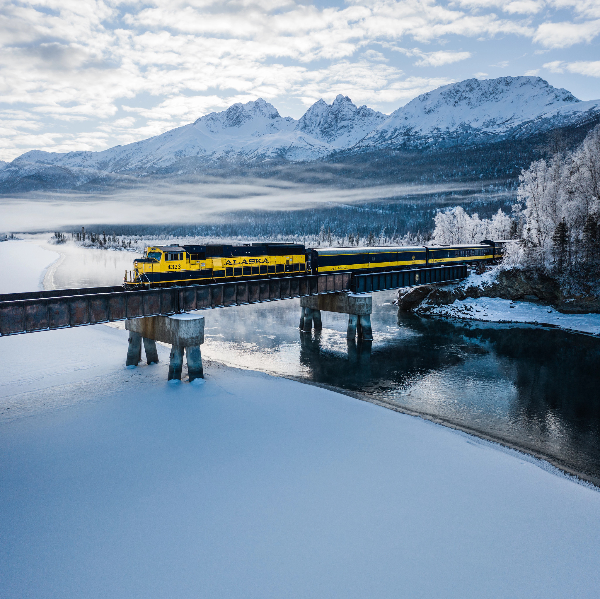 a train on a bridge with mountains around it