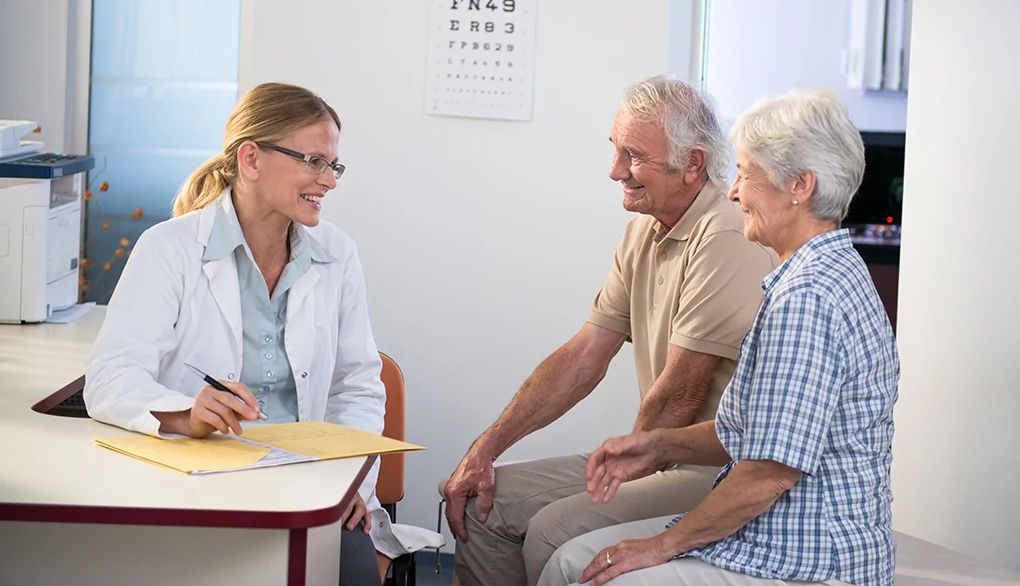 Medicare pays for an annual wellness visit with your doctor A man and woman speaking with a female doctor at a desk