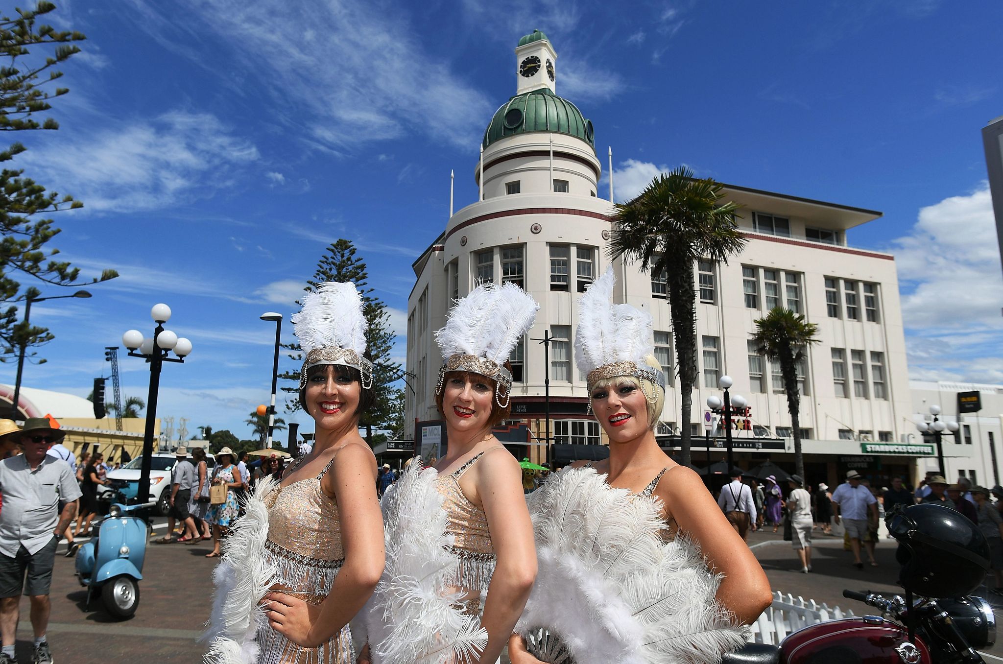 Visit These Cities to See the Art Deco Aesthetic three people, dressed as 1920s dancers, posing in front of an art deco building