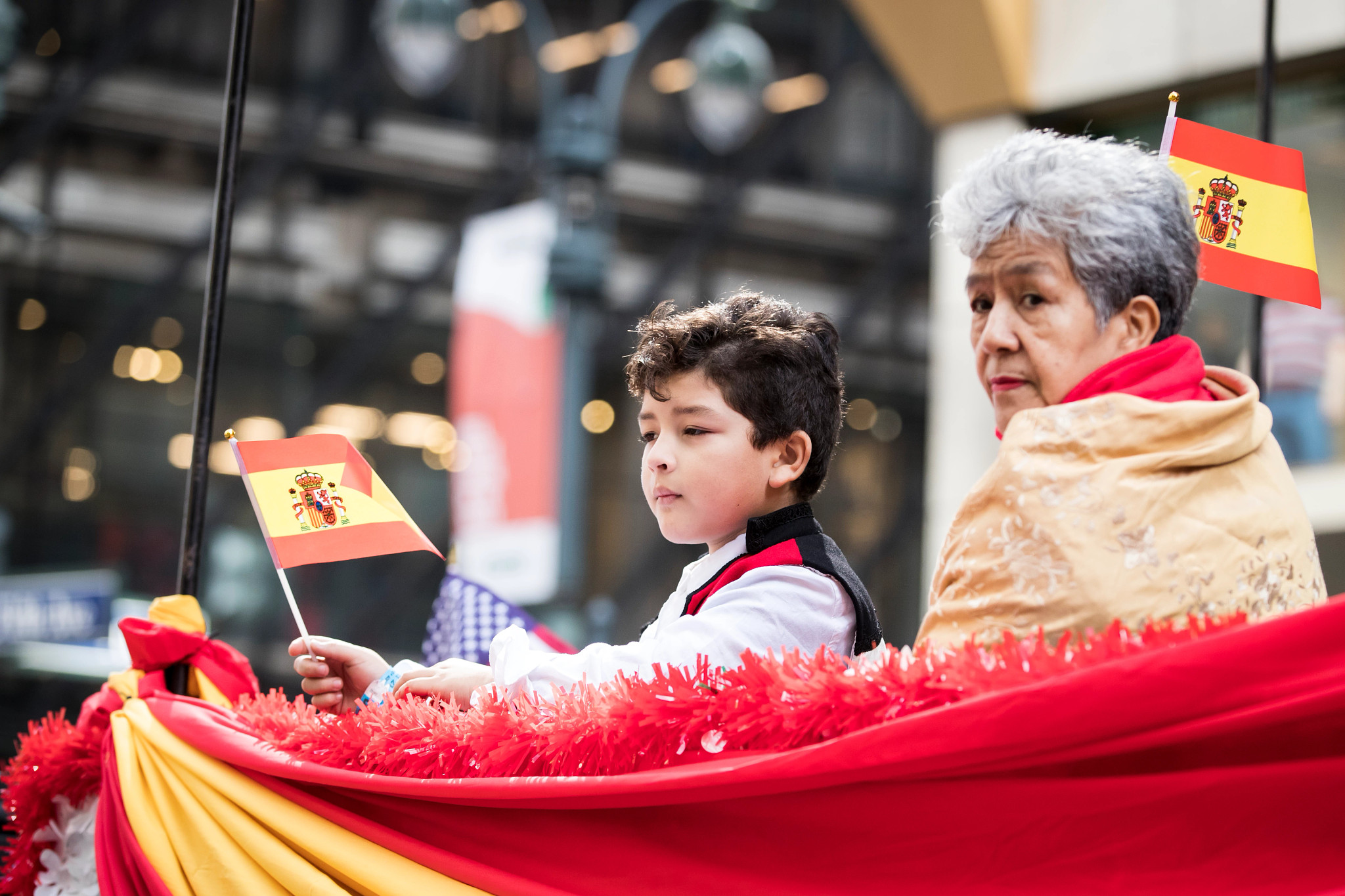 Una mujer y un niño sostienen banderas en el Desfile del Día de la Hispanidad