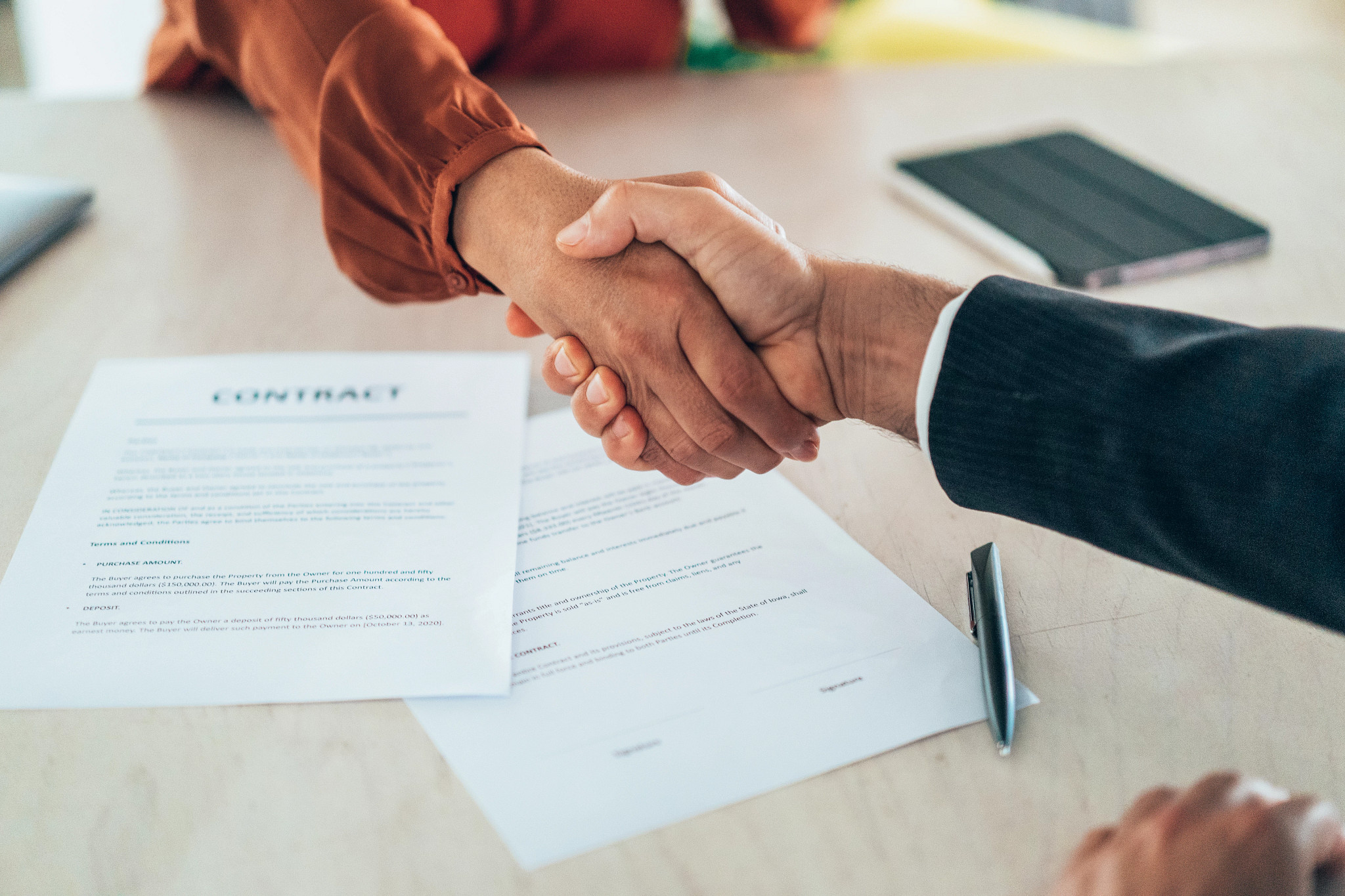 Two people shaking hands over a contract