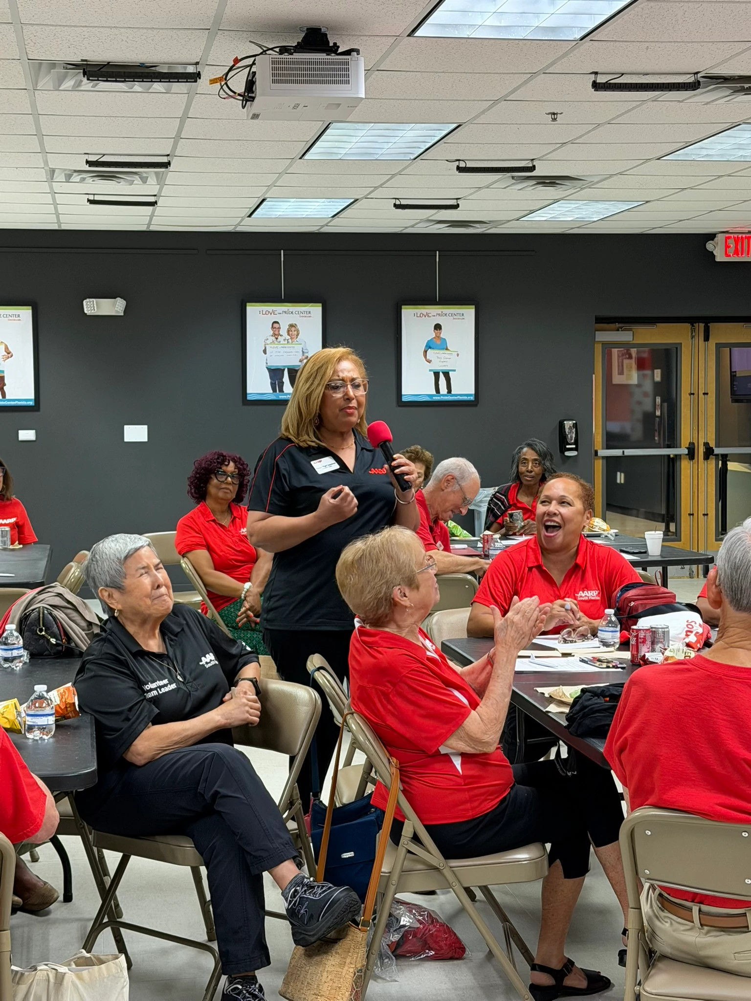 aarp volunteer event. people sitting at round tables and an aarp volunteer speaking on a microphone