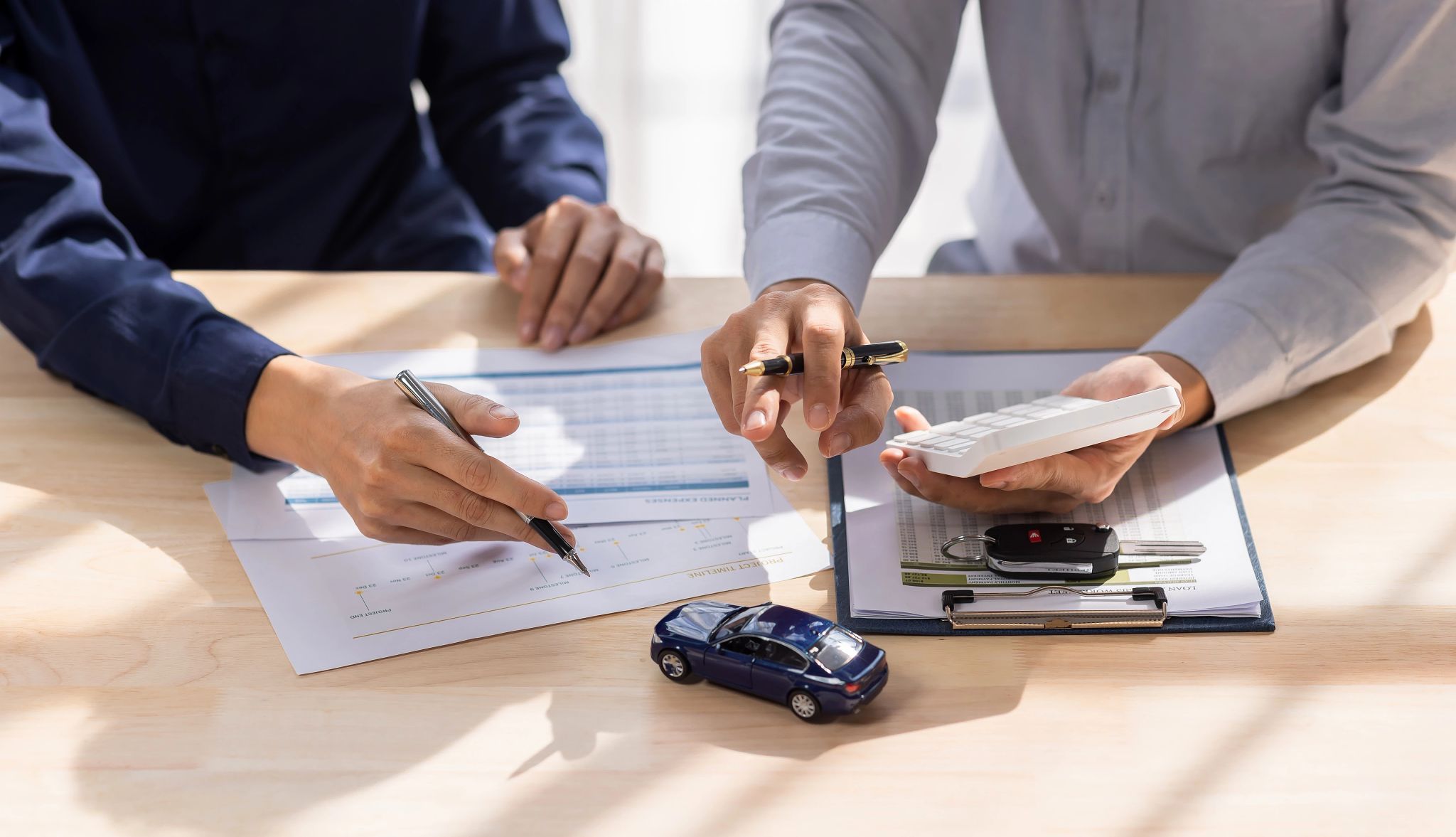 How to get started Hands of two people holding pens and calculator; papers, car keys and tiny car in front of them