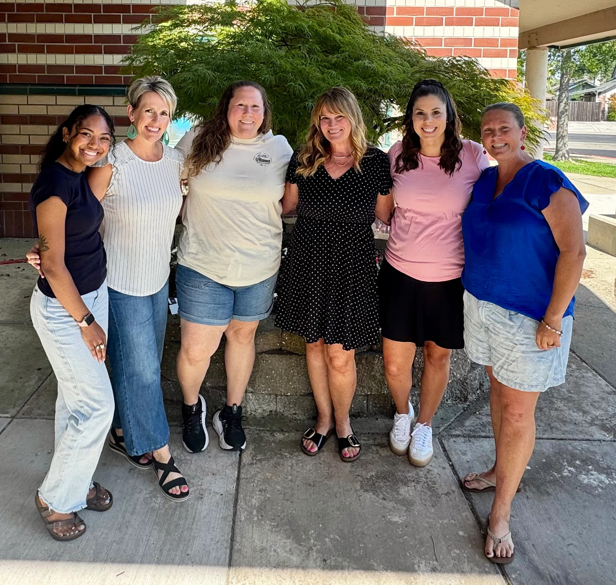 a group of women smiling and embracing while posing for a photo outside a building