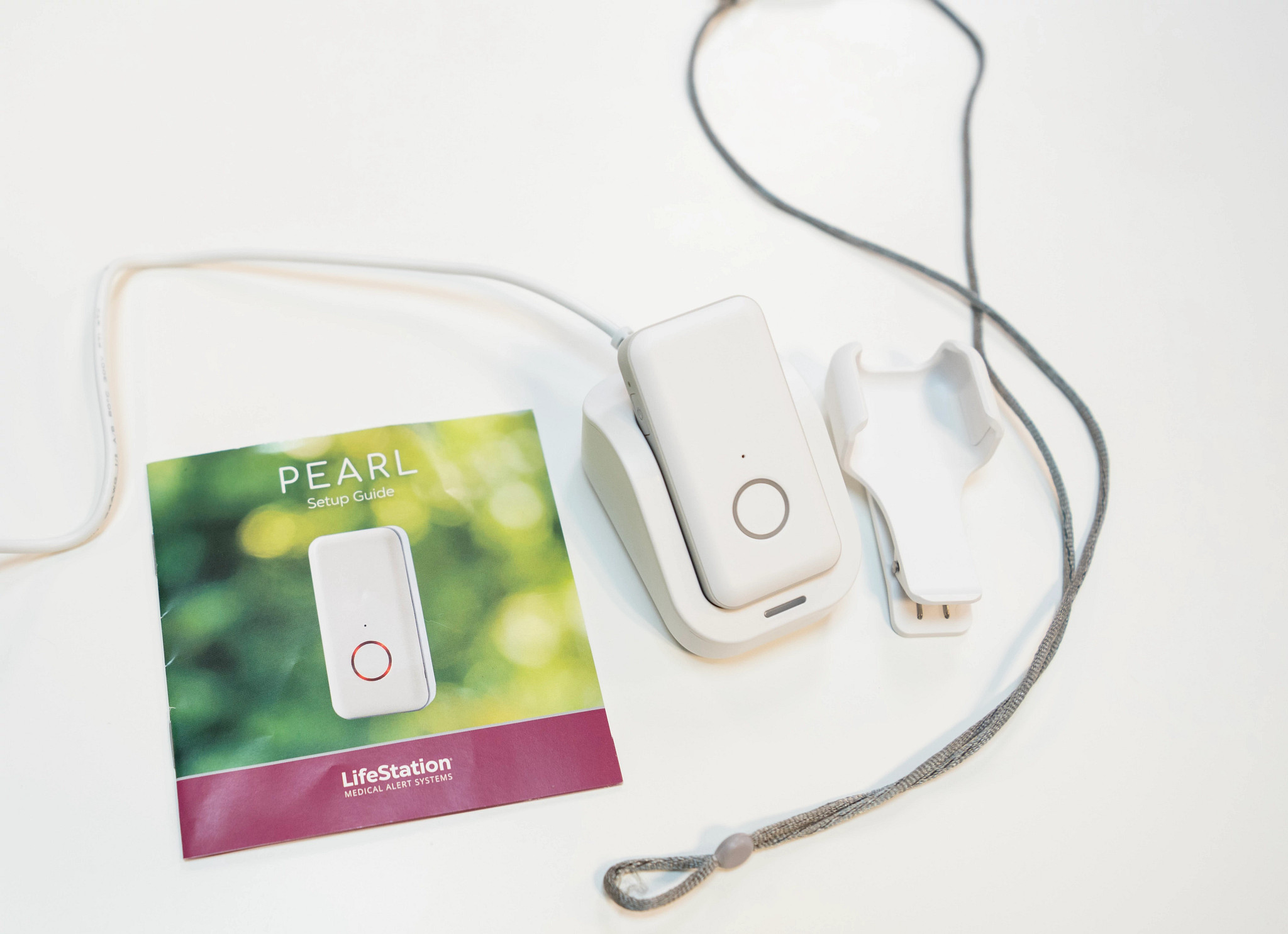The LifeStation Pearl pendant device on a white table next to the manual and belt clip.