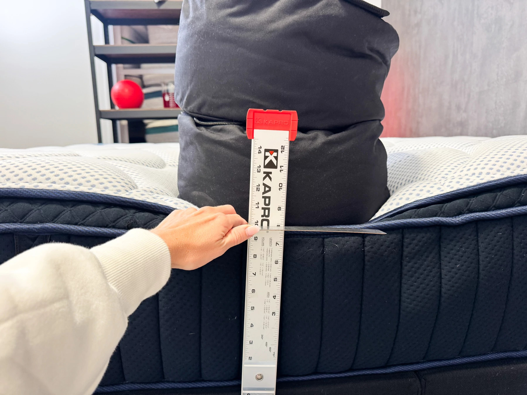 A woman measuring the sinkage of the DreamCloud Hybrid mattress under the weight of a 150-pound sandbag.