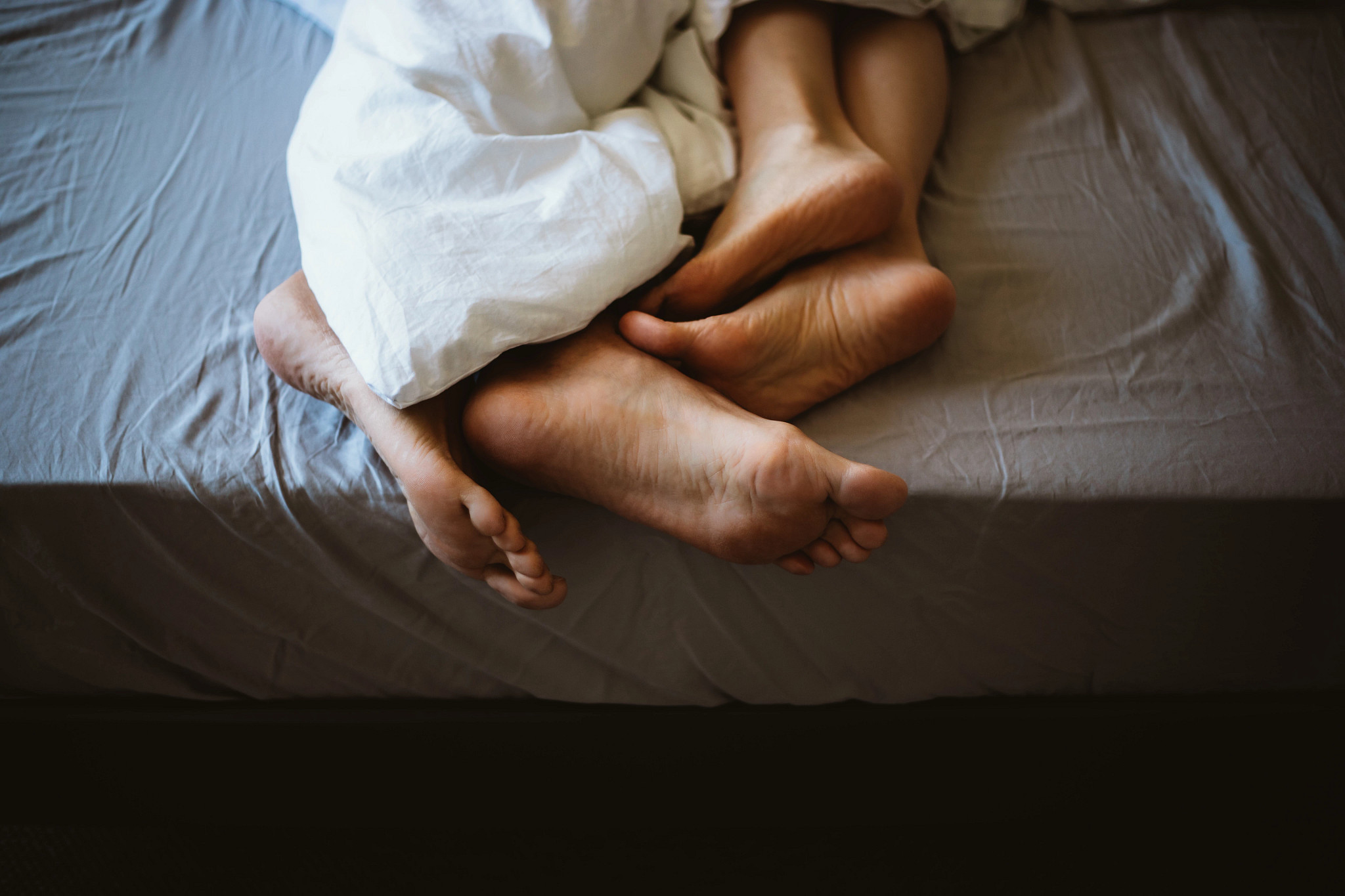 a photo shows a couple’s feet as they snuggle under the covers