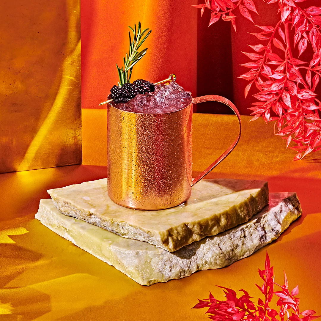 Copper mug filled with a purple mocktail garnished with rosemary and blackberries