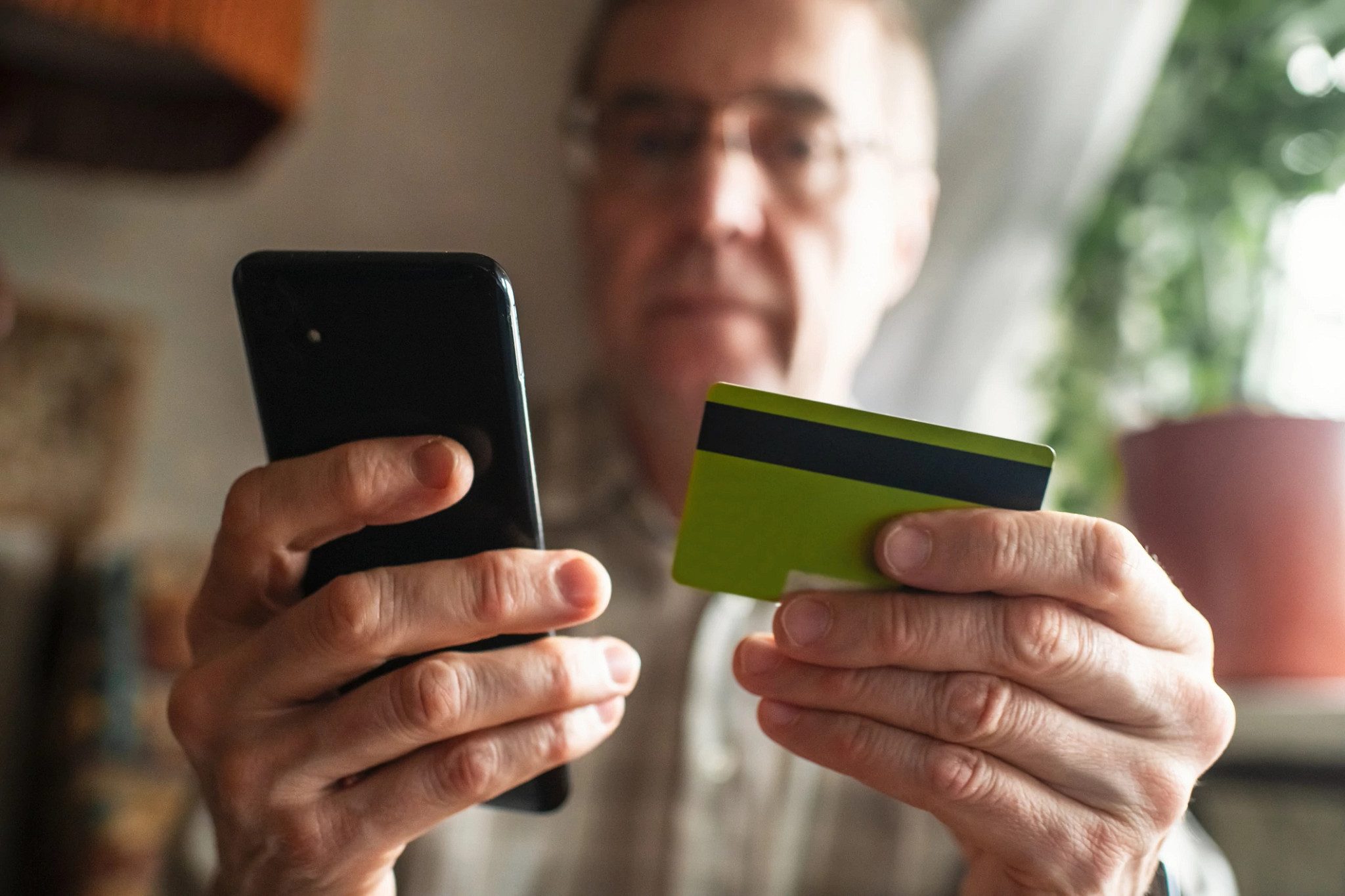 Senior man with smartphone and credit card at home