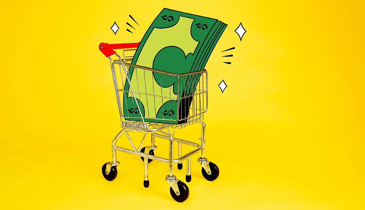 Giant dollar bills in a shopping cart on a yellow background.