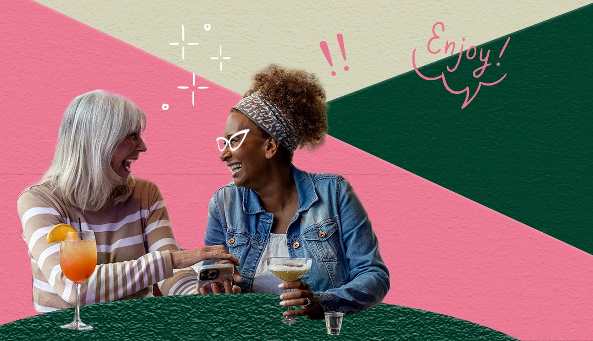 Lifestyle photo with two people seated at a table holding cocktails and looking at a smartphone, set against a colorful graphic background, created for healthy aging content for women 50+, older women, active retirement, friendship, and social connection.