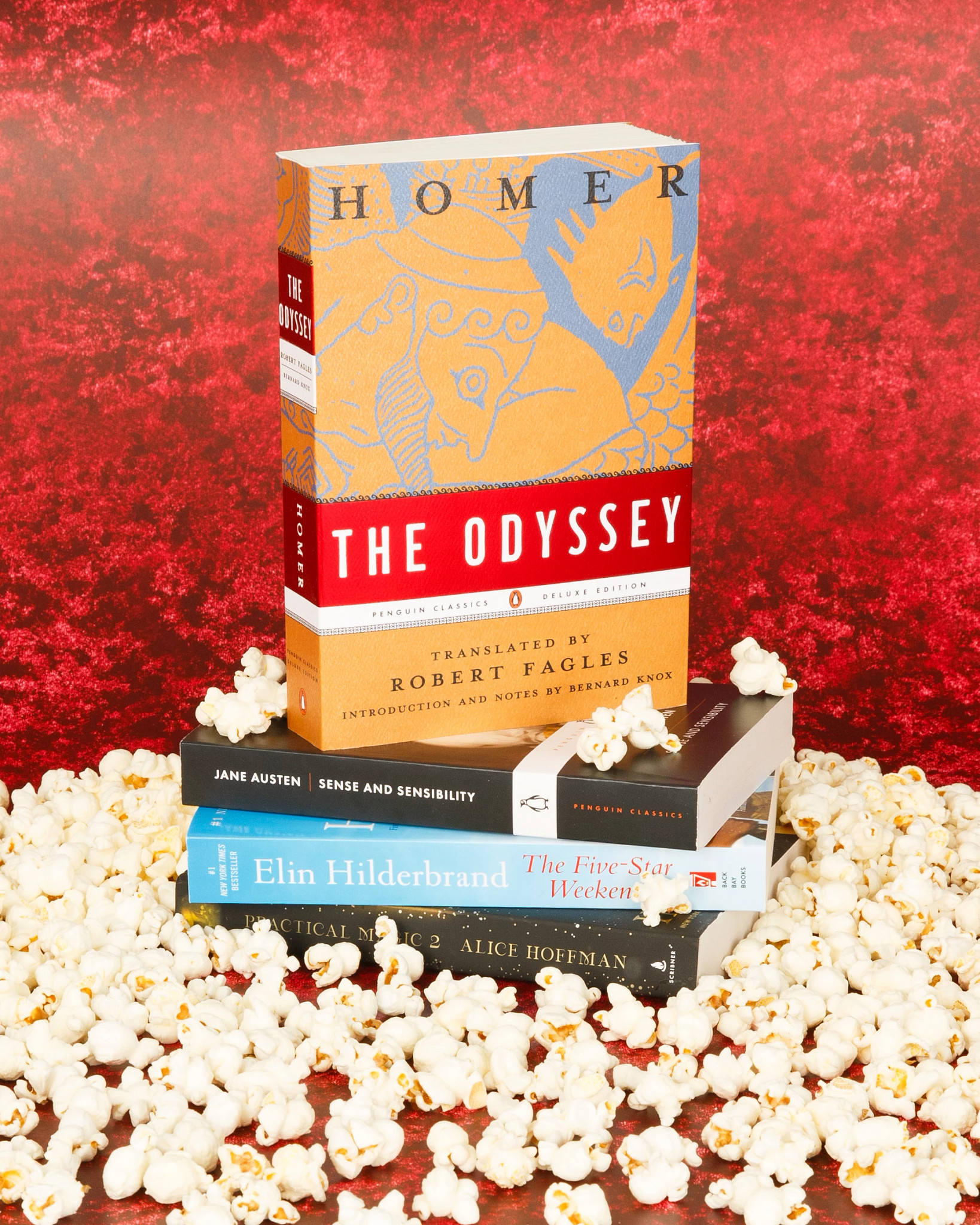 A stack of books featuring The Odyssey, surrounded by scattered popcorn on a textured red background