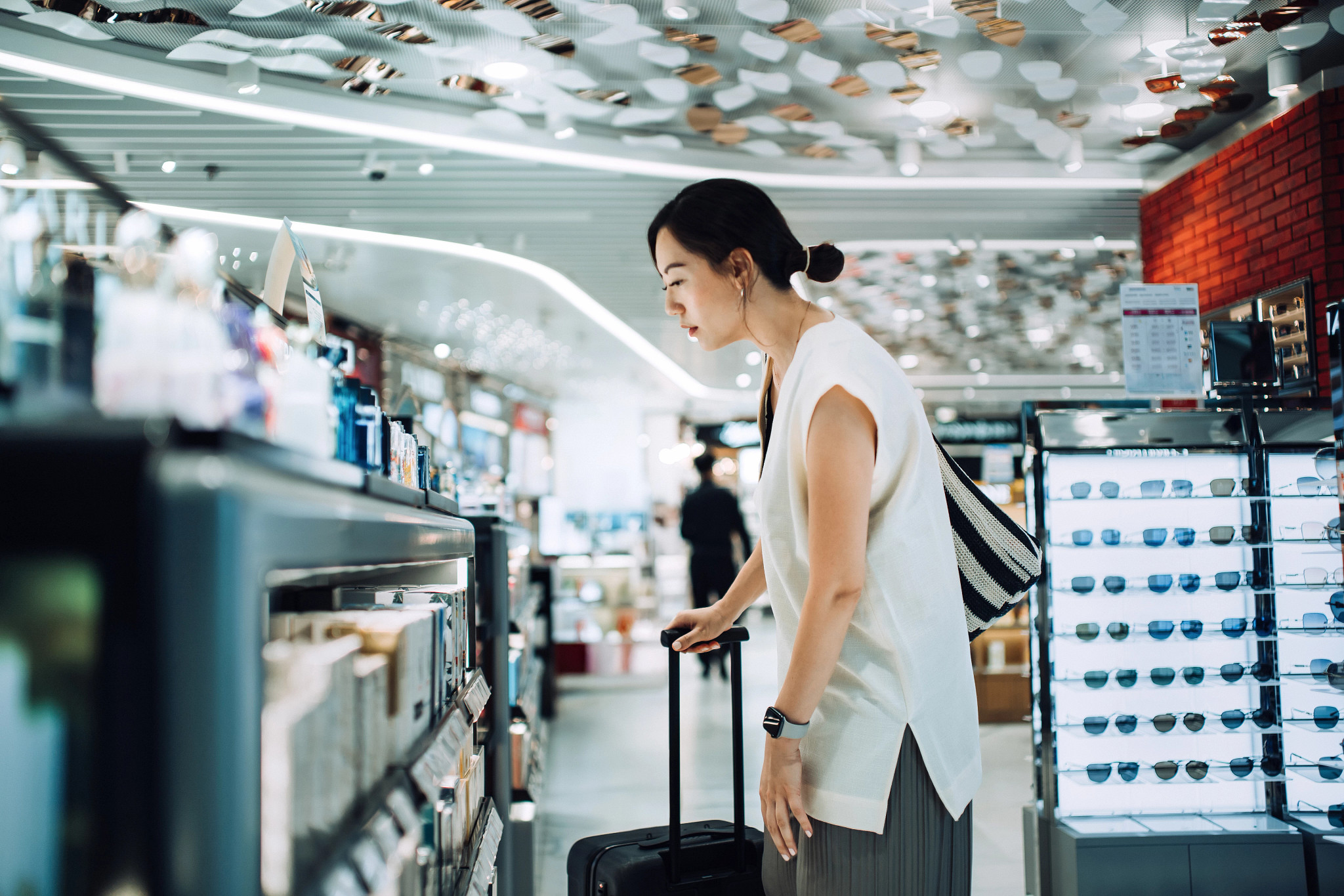 a woman carrying a suitcase shopping at a duty free shop in an airport