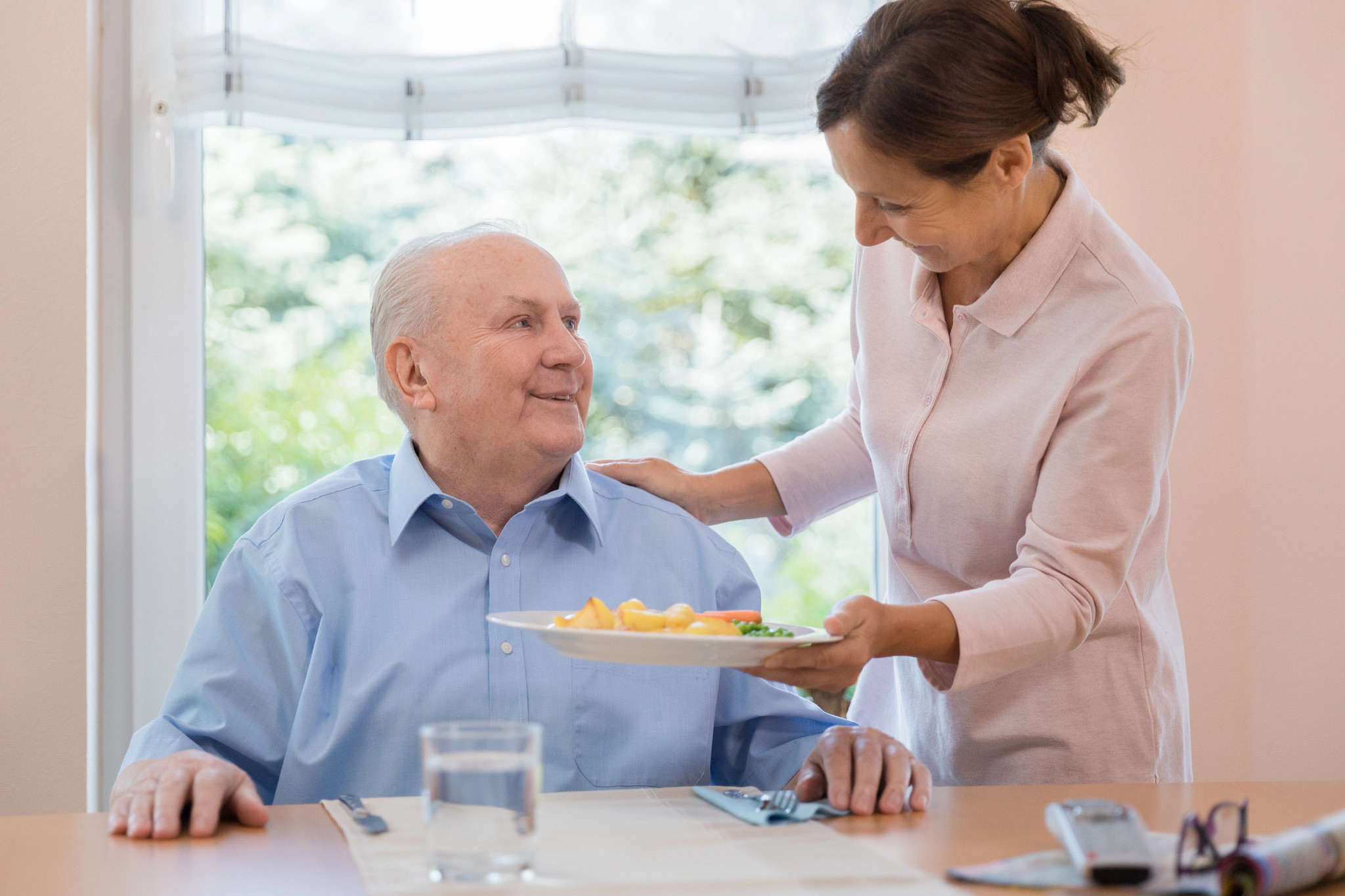 A woman smiling as she serves a meal to an older man