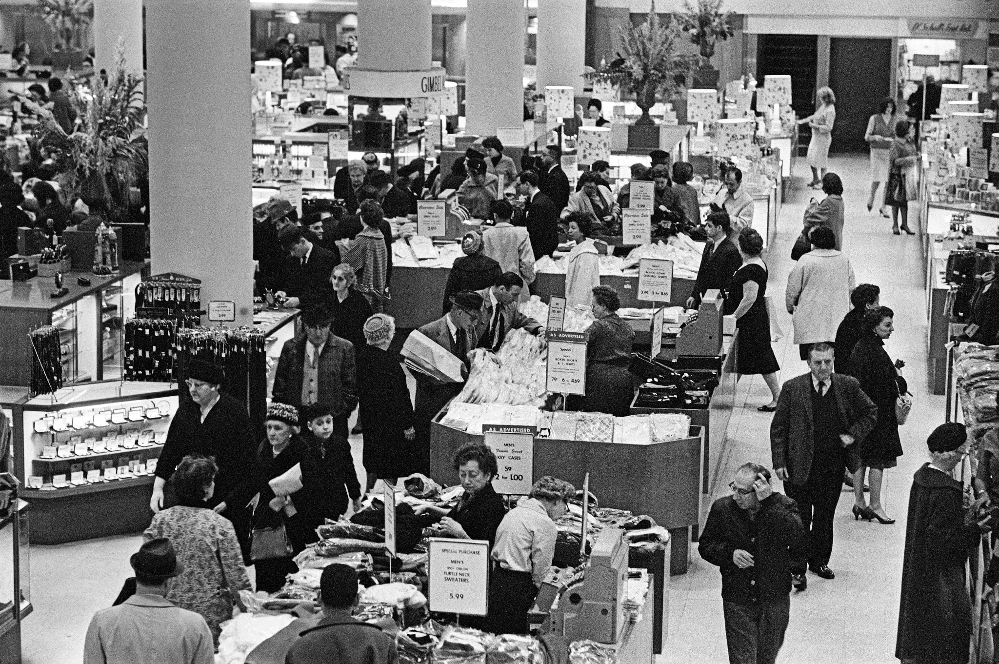foto en blanco y negro de compradores buscando productos en contenedores dentro de una tienda 