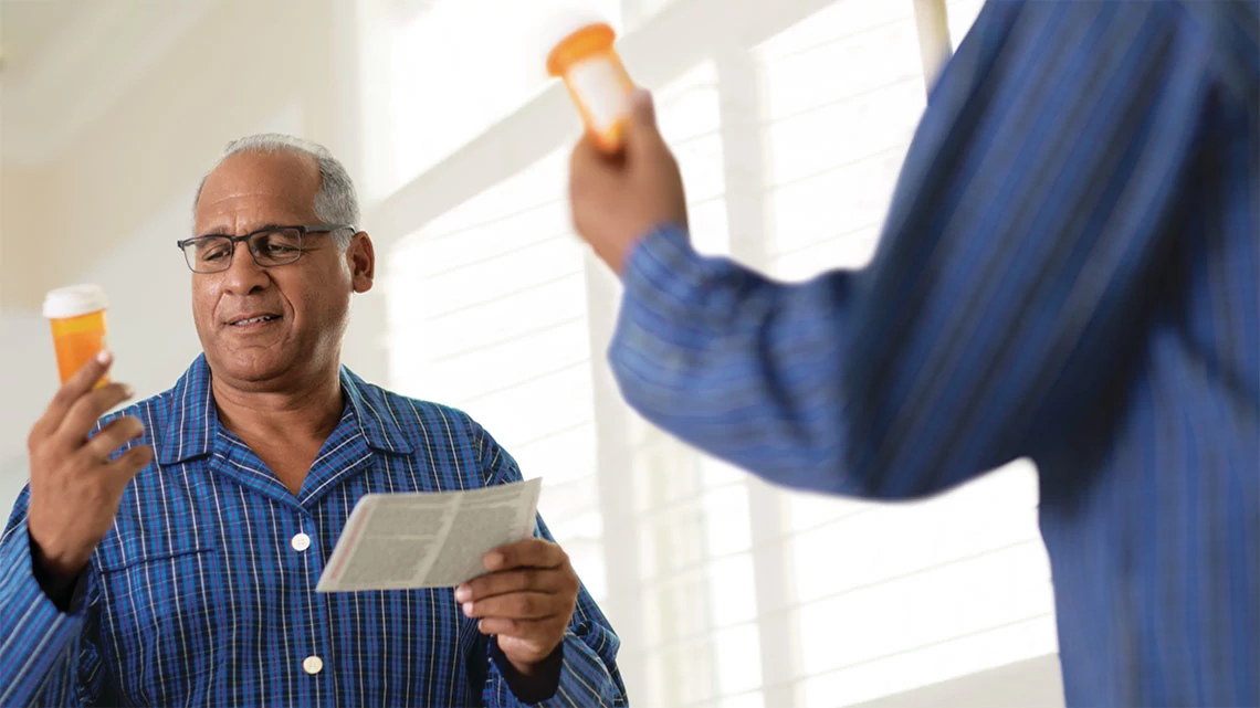  older man in pajamas looking at pill bottle reading instructions