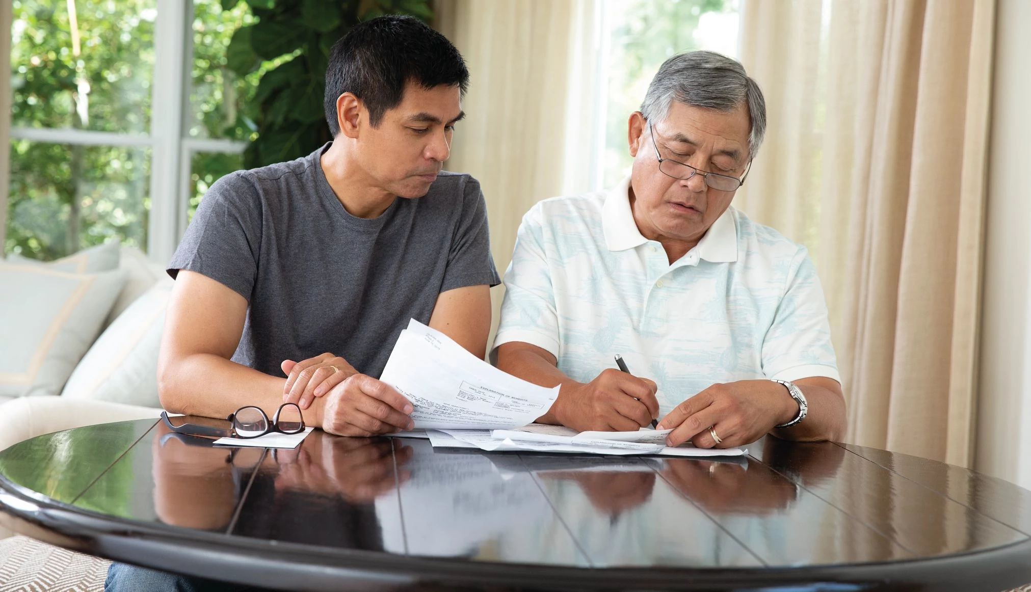 Adult male sitting beside older adult male at a table while looking through paperwork