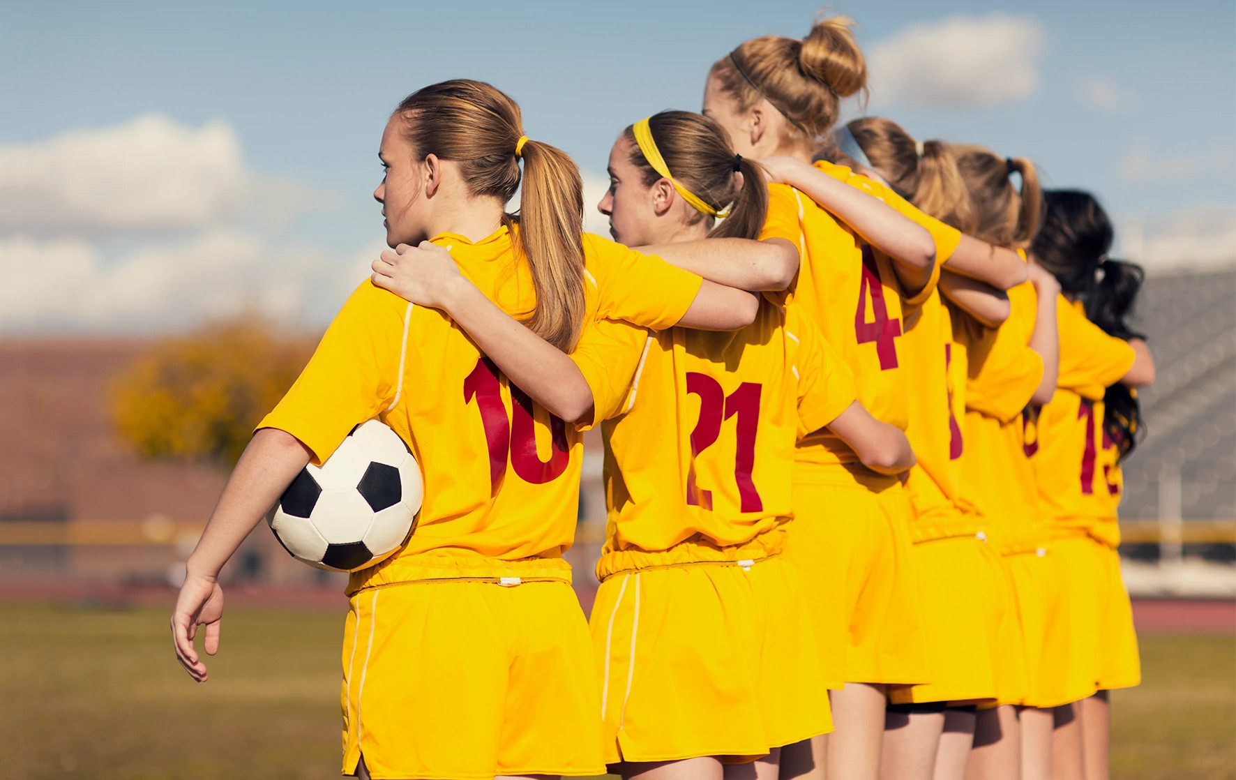 Young girls playing soccer standing on the sidelines arm and arm before the game