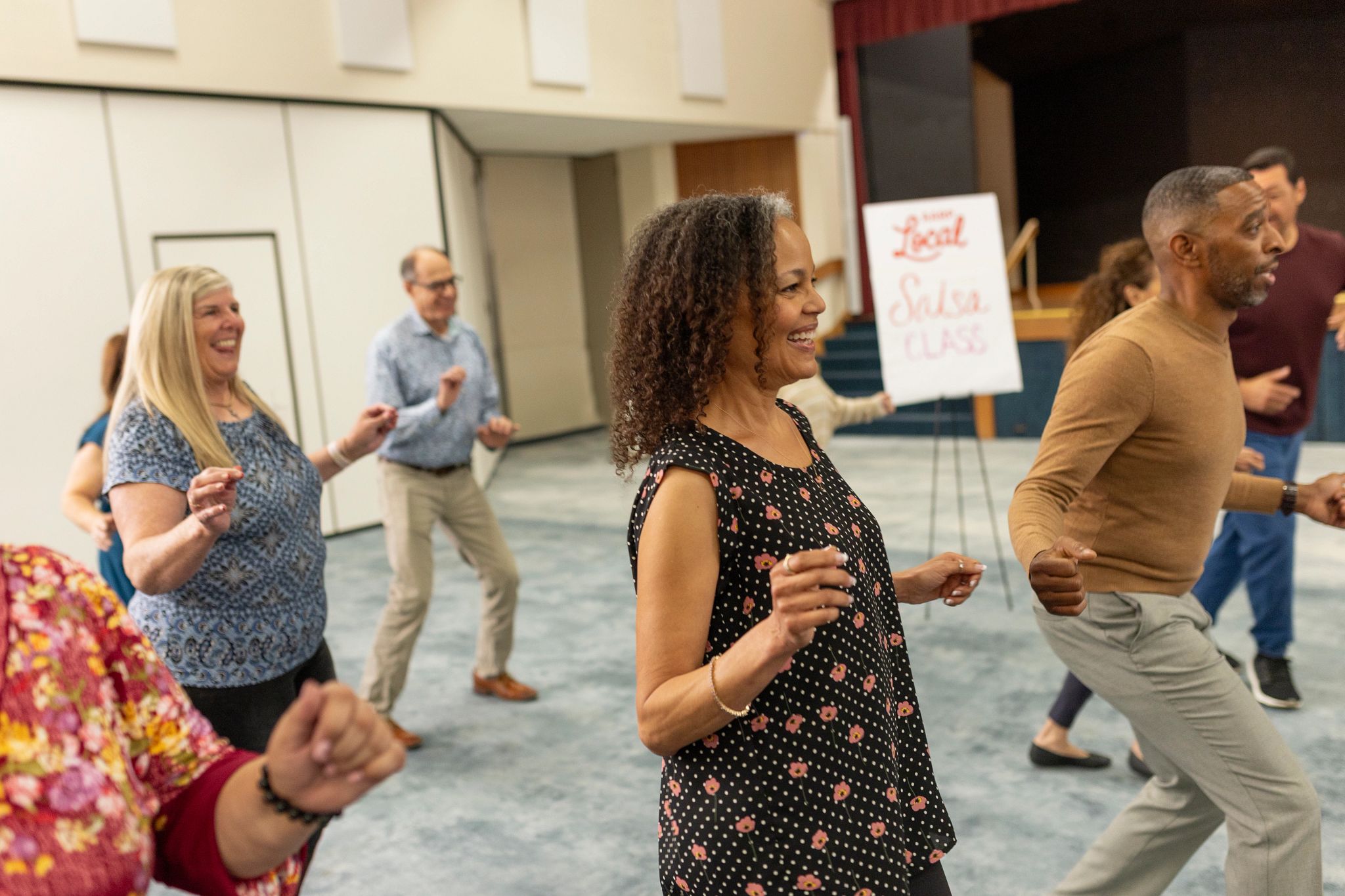 Participants practice salsa dance steps during an AARP Local class that combines fitness, learning, and social engagement in a community setting.