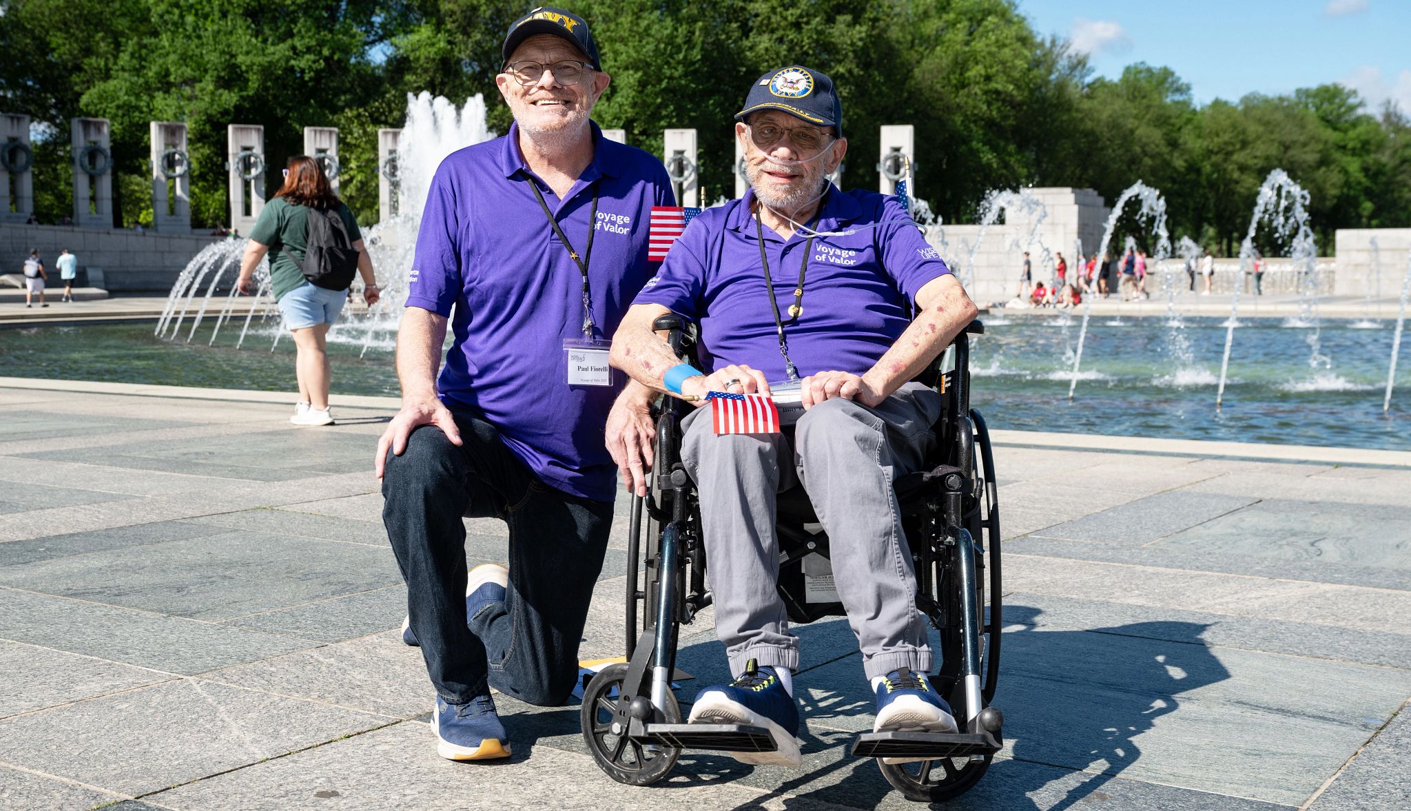 LGBTQ Veteran Finds Closure Through Wish of a Lifetime Billy Fiorelli sitting in a wheelchair in front of the World War Two Memorial fountain while his husband kneels beside him