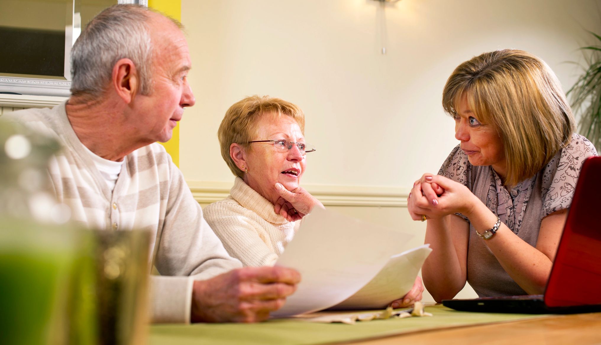 a caregiver sits at a table with an older couple, helping them fill out paperwork