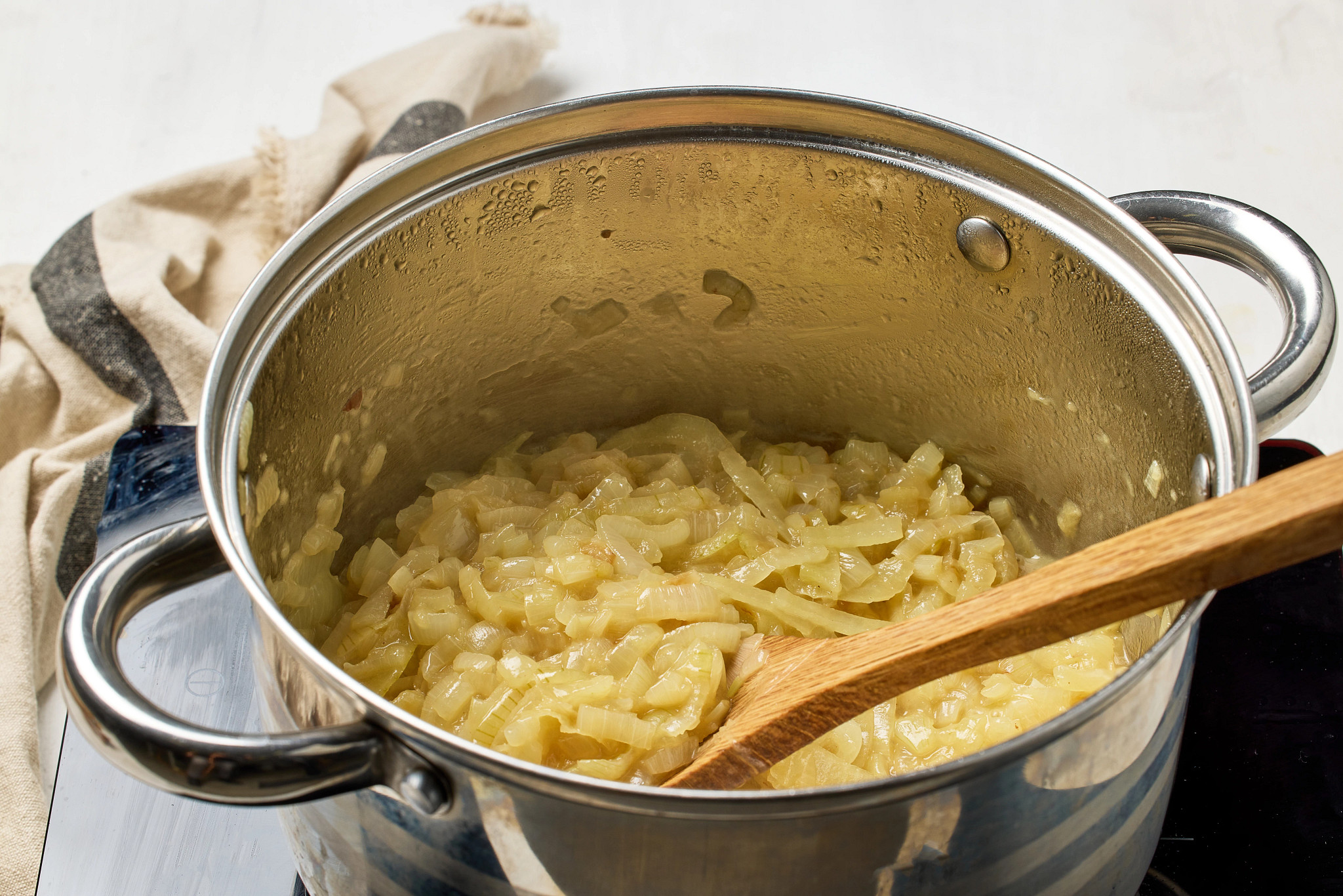 Close-up of caramelized onions cooking in a stainless-steel pot with a wooden spoon