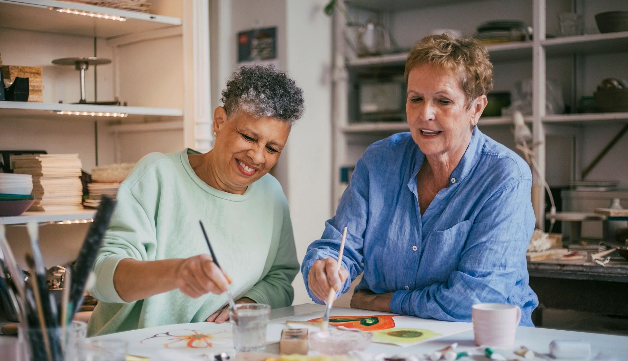 Smiling woman talking to friend while painting in workshop Smiling woman talking to friend while painting in workshop