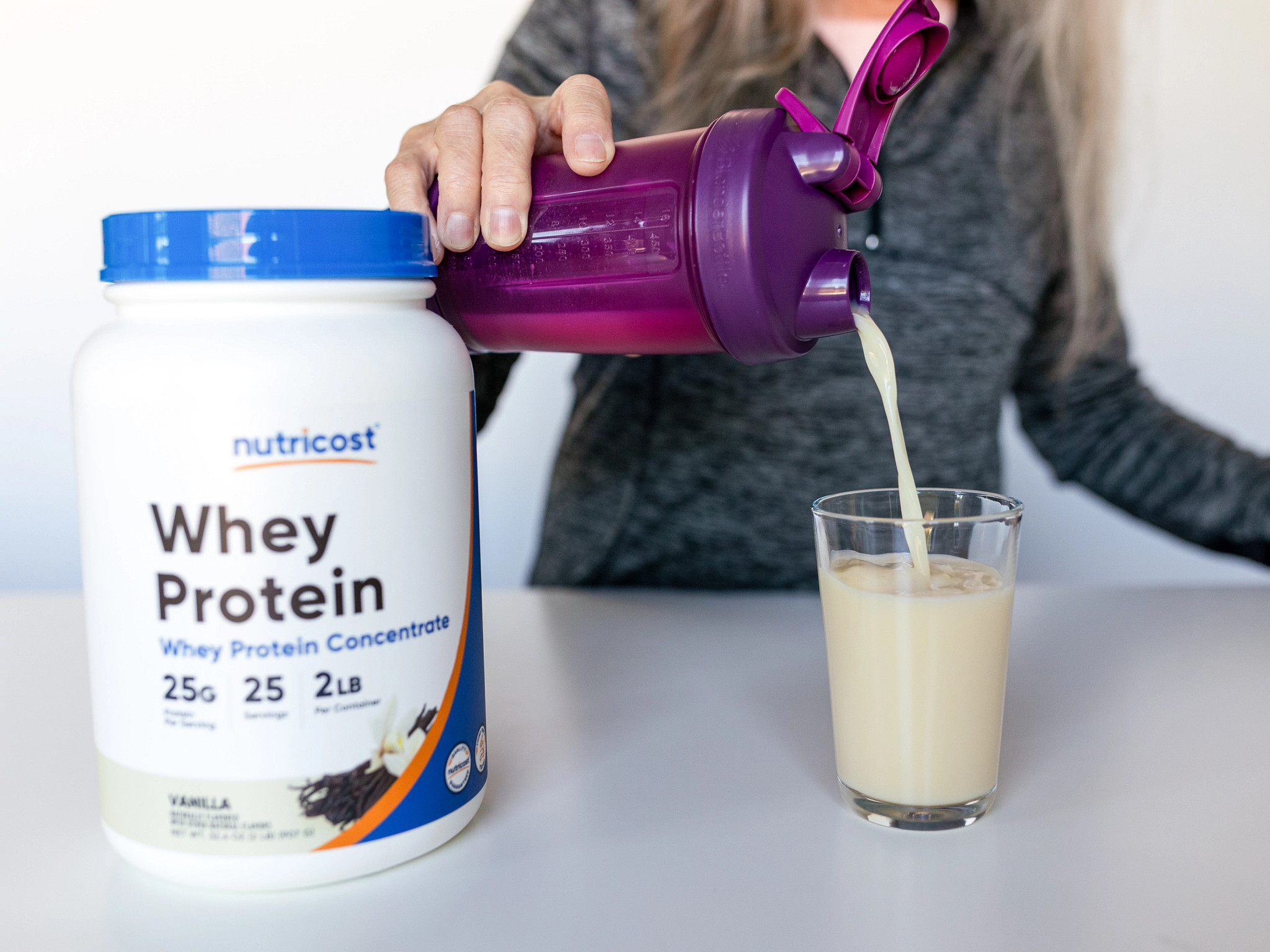 A person pours Nutricost Whey Protein Concentrate drink from a shaker bottle into a glass