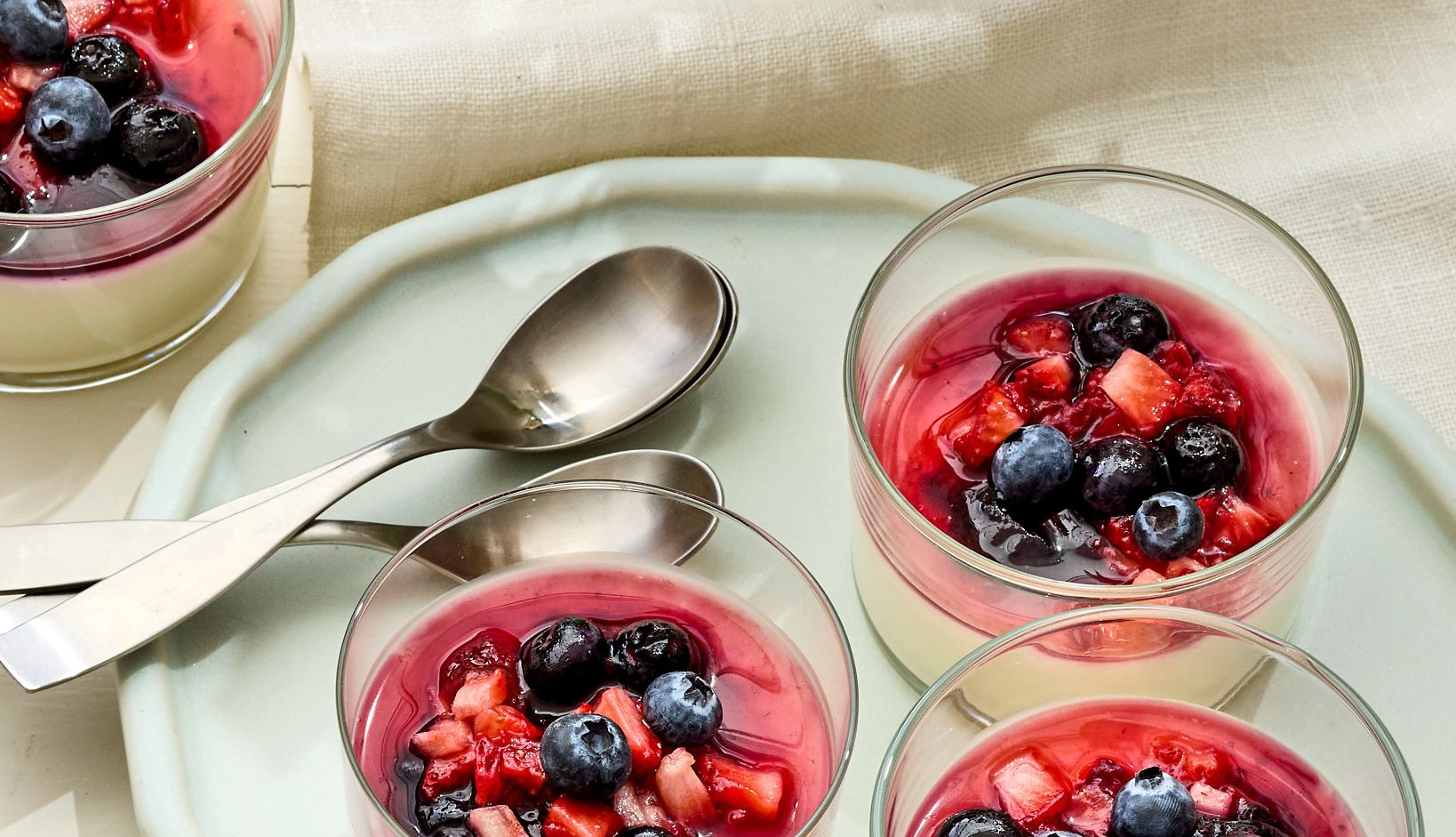 Yogurt Panna Cotta With Red and Blue Berries Three Yogurt Panna Cotta With Red and Blue Berries desserts are pictured on a plate with two spoons. Off the plate on the left side sits another.