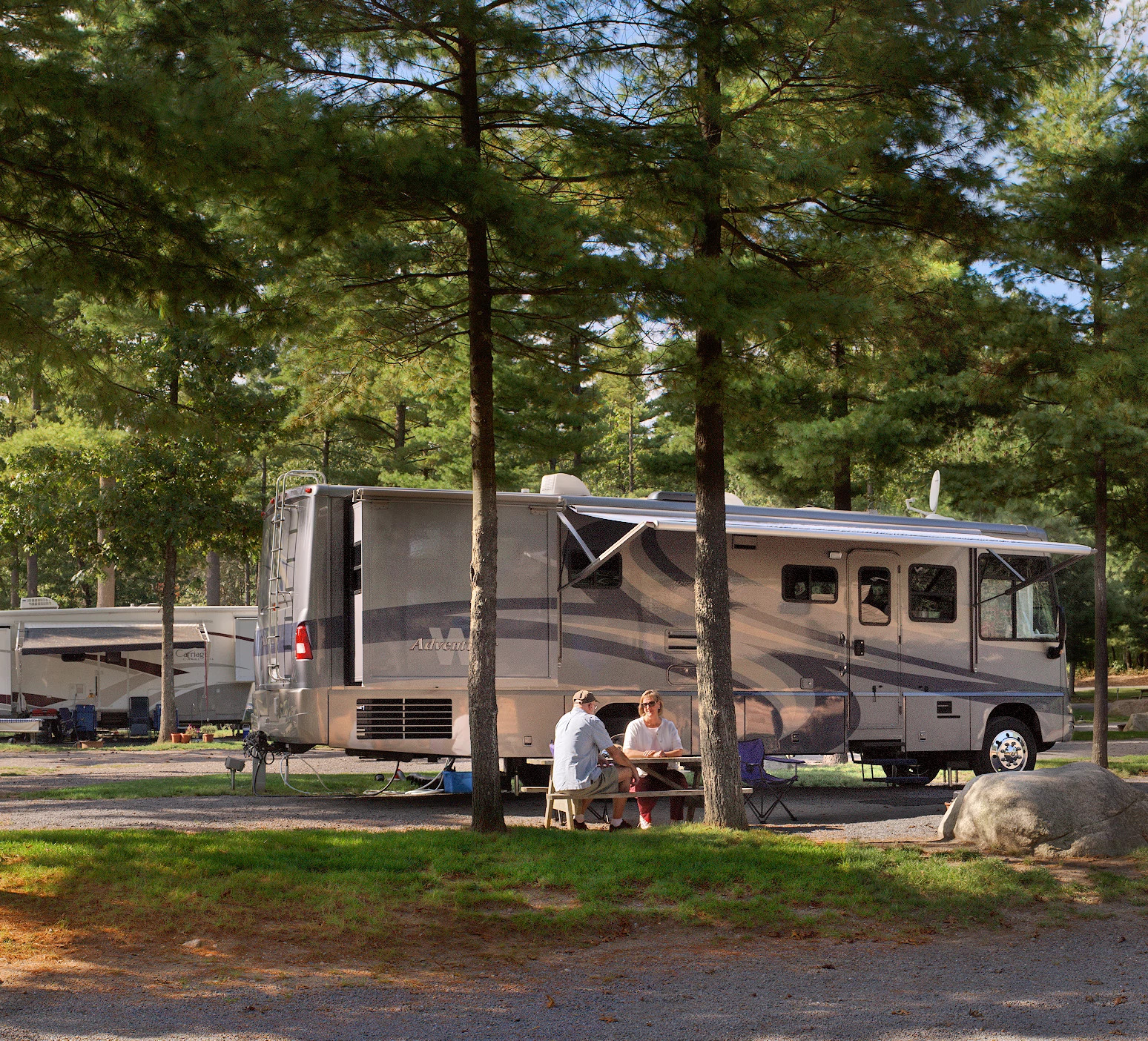 people sitting at a table outside of an RV at a campsite