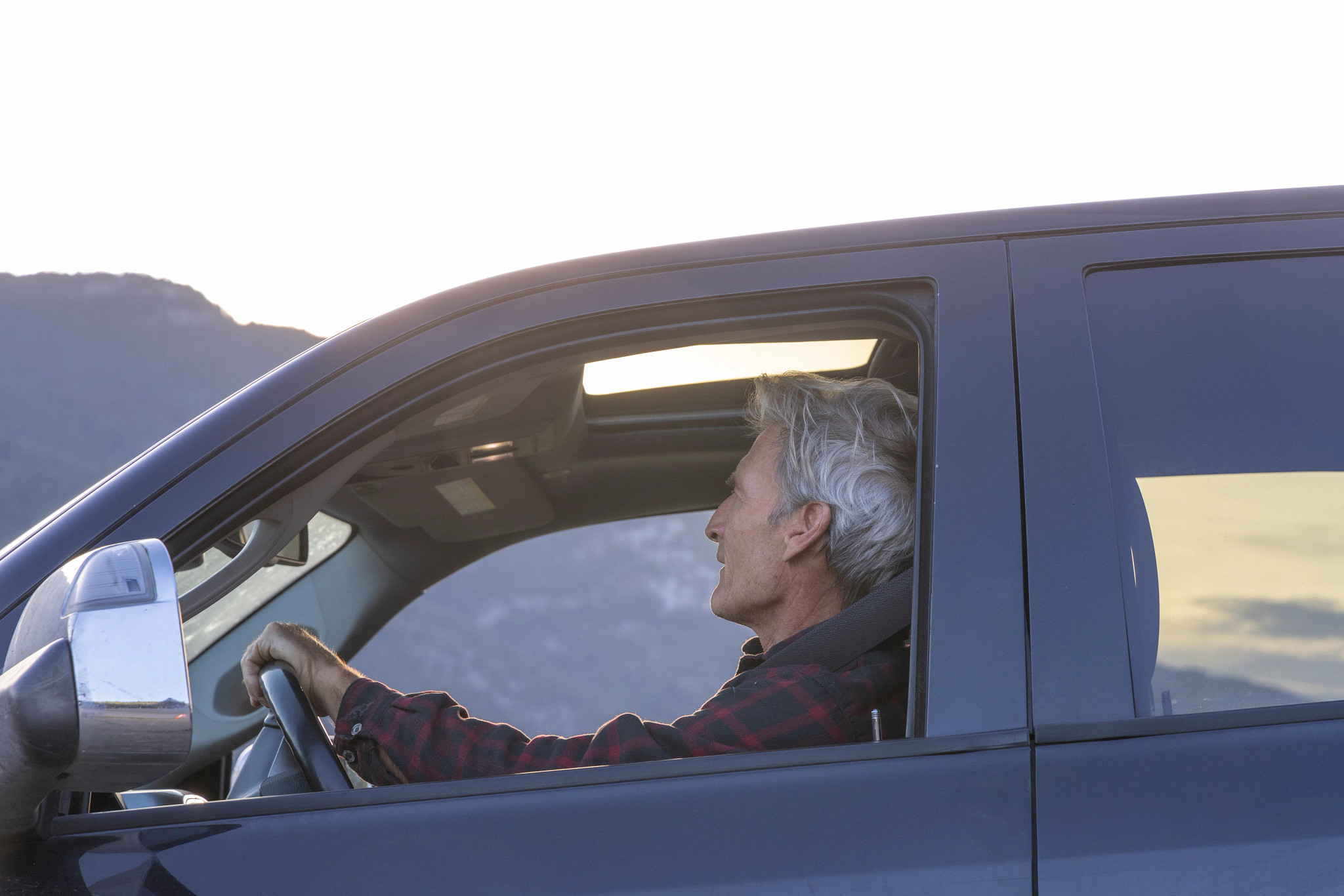 Mature man drives down mountain road, at sunrise