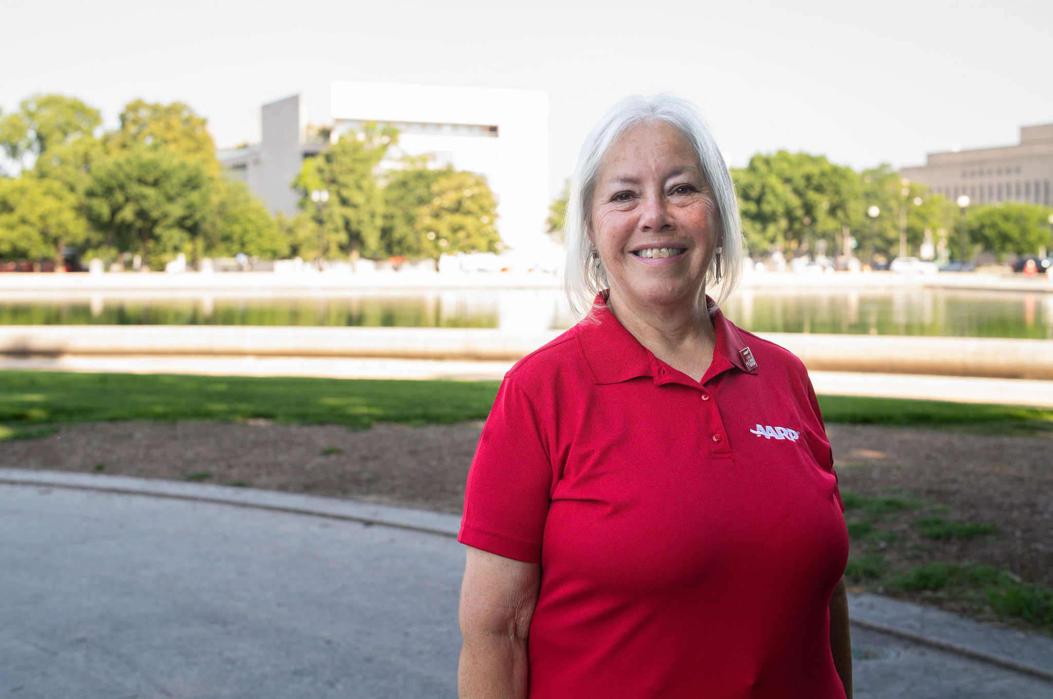 a woman standing outside with a red AARP shirt poses for a picture