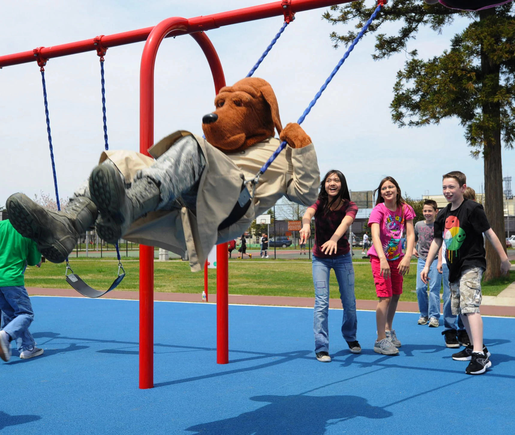McGruff is shown in a photo being pushed on a swing set by several kids