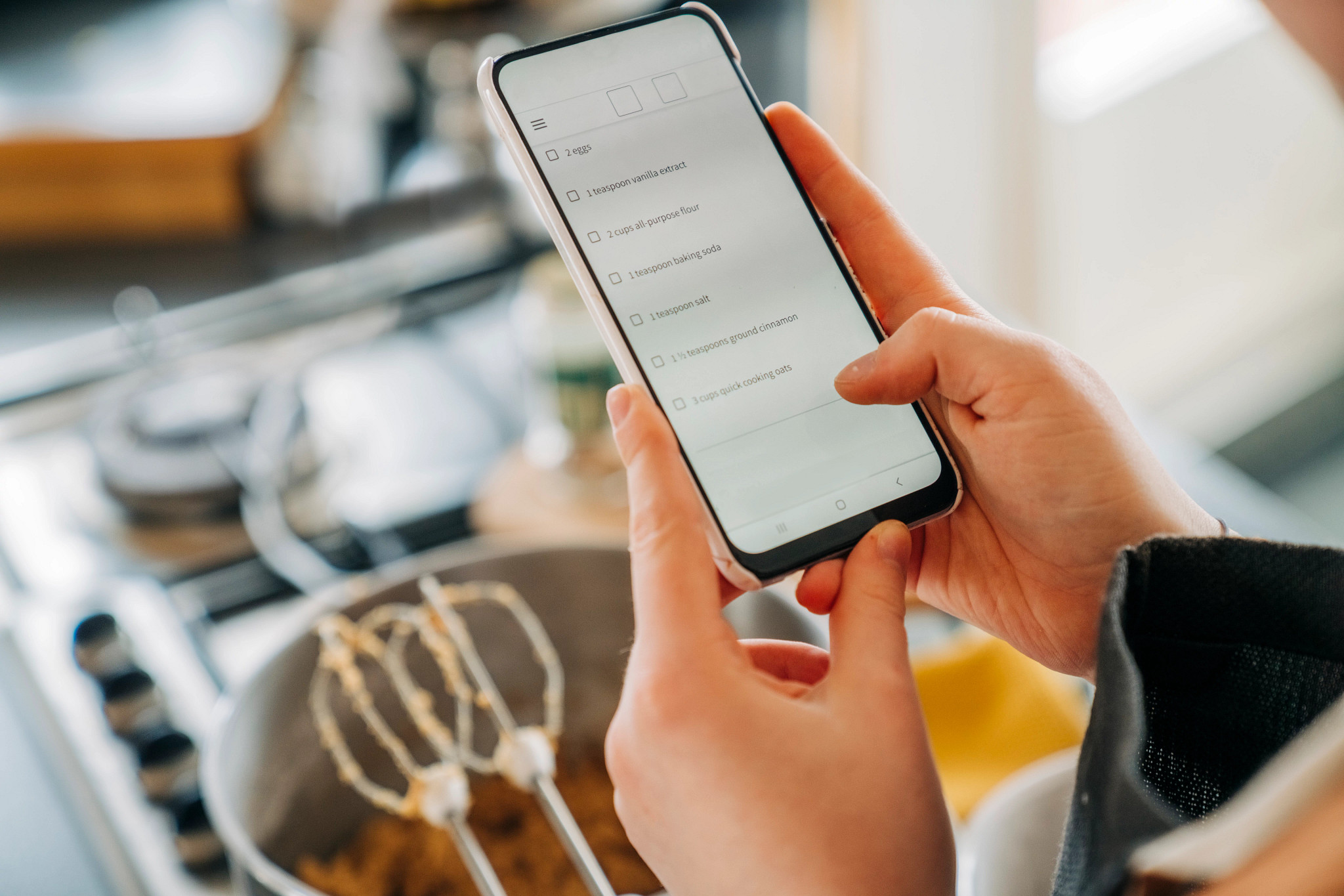 Person holding mobile phone in kitchen preparing for cooking searching online recipe for information about ingredients. Homemade meal in preparation with help from internet cookbook