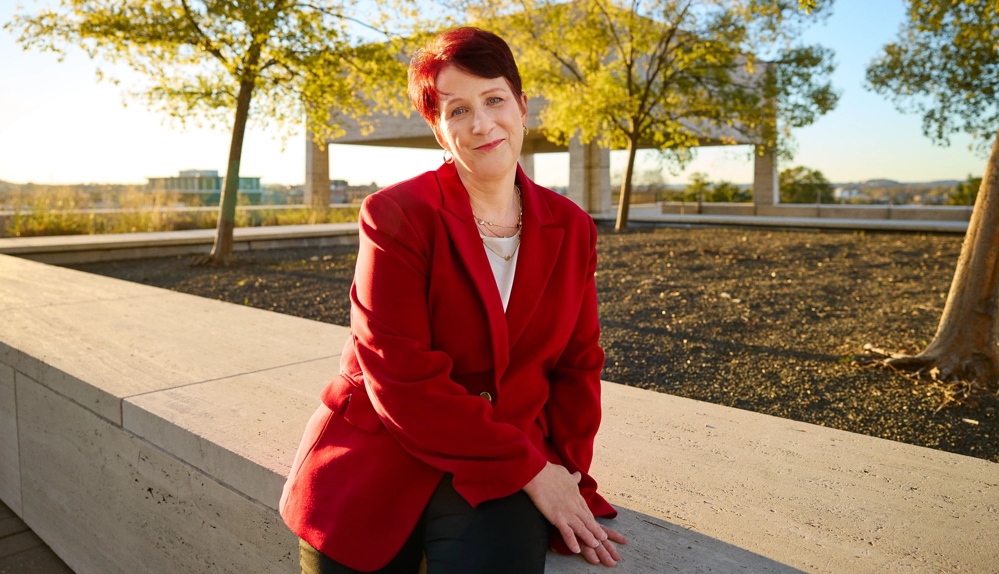 A potrait of unsung nursing home hero Outdoor portrait of a Melinda Lunday, dressed in a bold red jacket, against a backdrop of urban greenery.