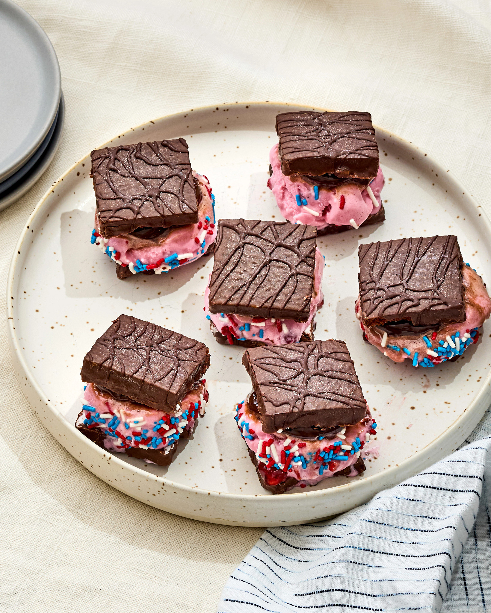 Five Independence Day Ice Cream Sandwiches are pictured on a plate, with red, white and blue sprinkles on the filling.