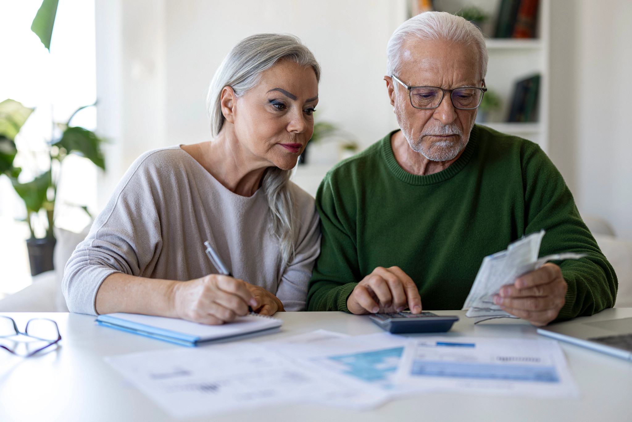 an older adult couple is sitting at a table going through some receipts with a calculator