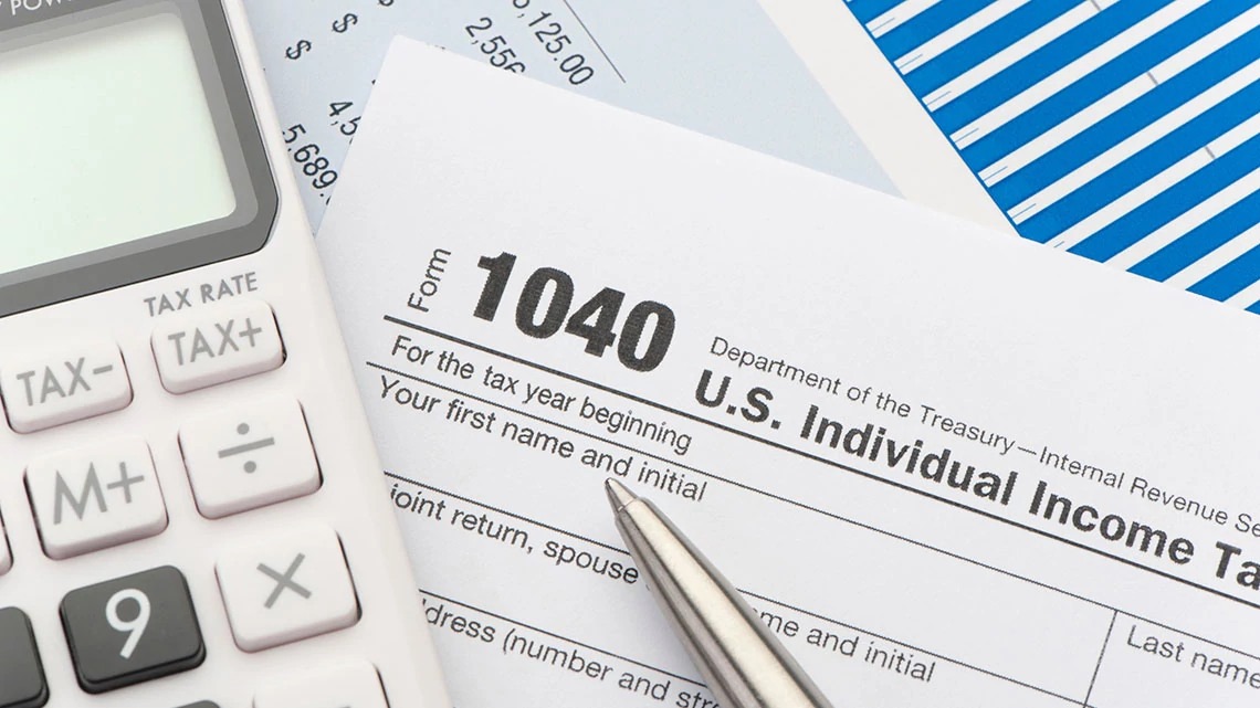 1040 Income Tax Calculator part of calculator with 1040 tax form and silver pen laying on it