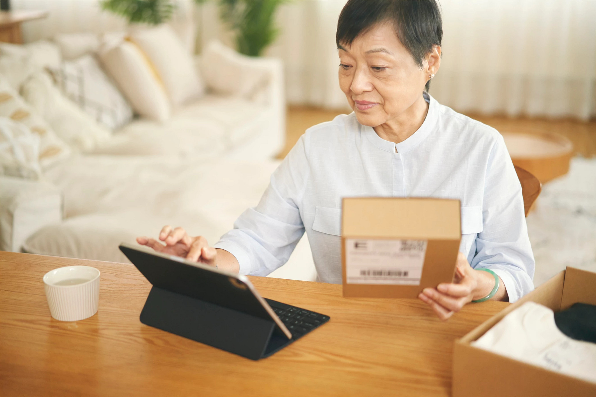 An elderly Chinese woman use a tablet to prepare shipping a parcel