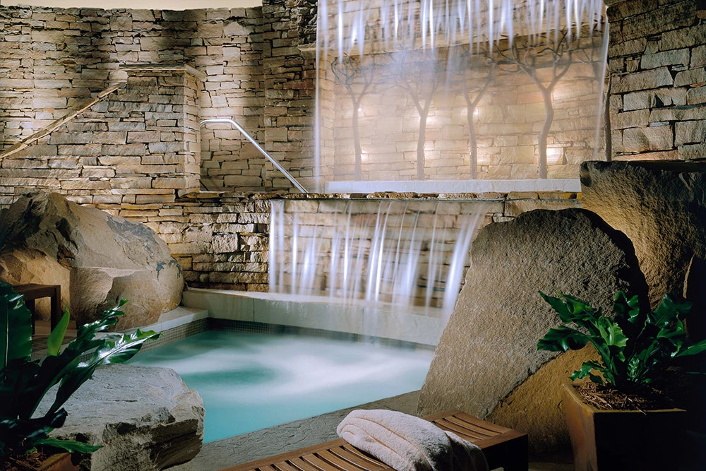 Indoor spa pool with cascading waterfall surrounded by natural stone walls and tropical plants in Pennsylvania