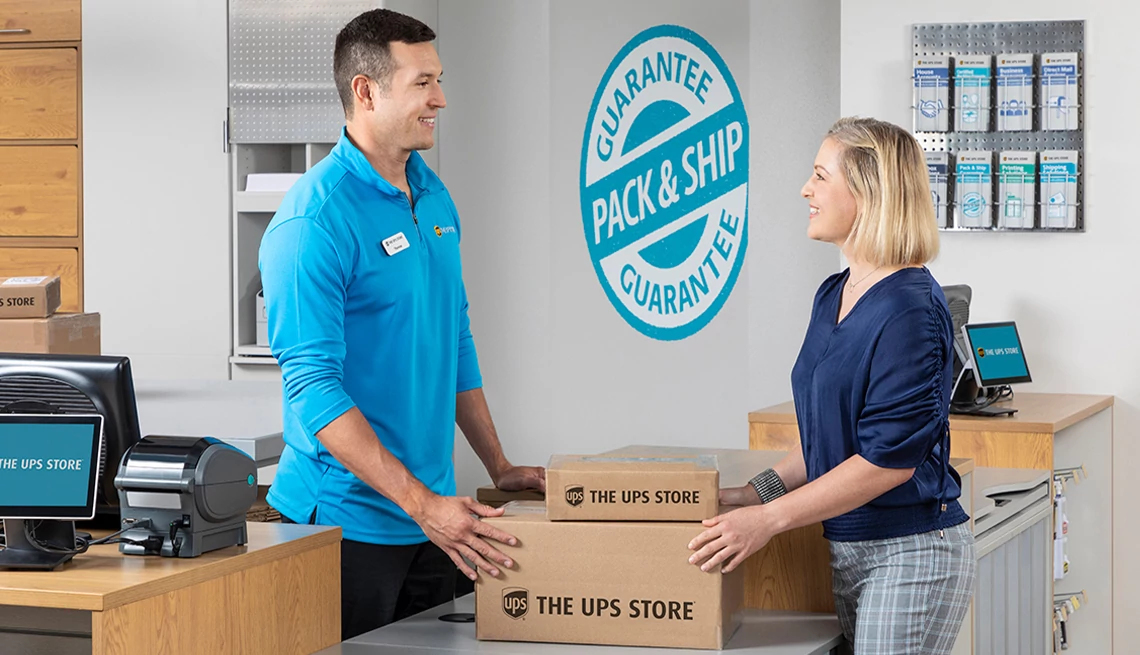 The UPS Store® Shipping Services Woman handing over packages to employee at The UPS Store
