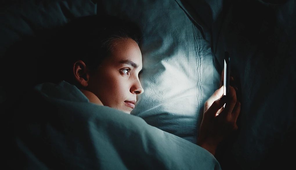 Insomnia is often an issue for adults A woman using phone while lying in bed in a dark room