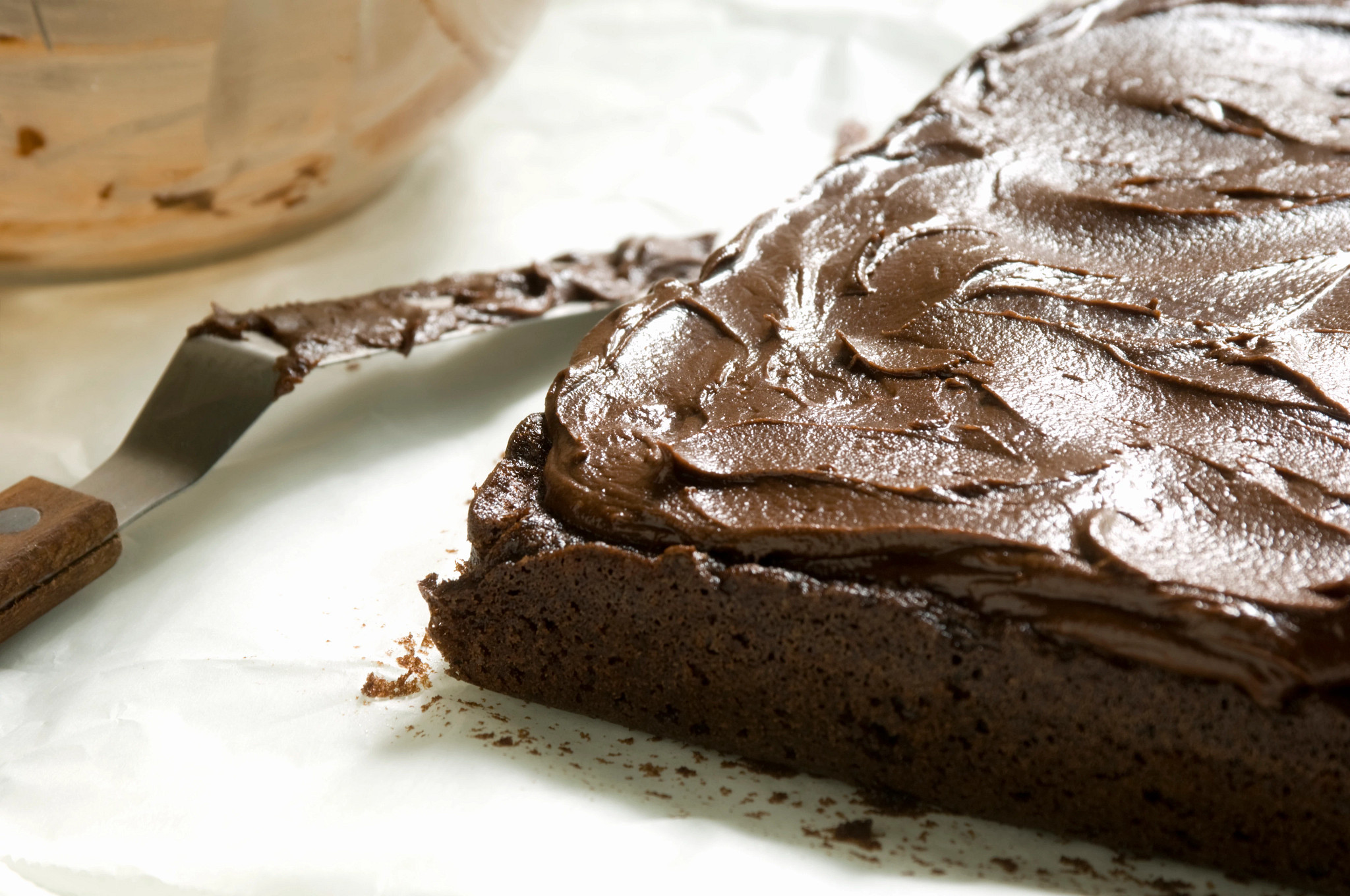 Close-up photo of a chocolate brownie topped with thick, glossy chocolate frosting spread smoothly across the surface