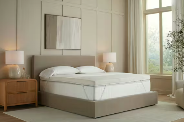 The Saatva Graphite Memory Foam Mattress Topper strapped to a white Saatva mattress