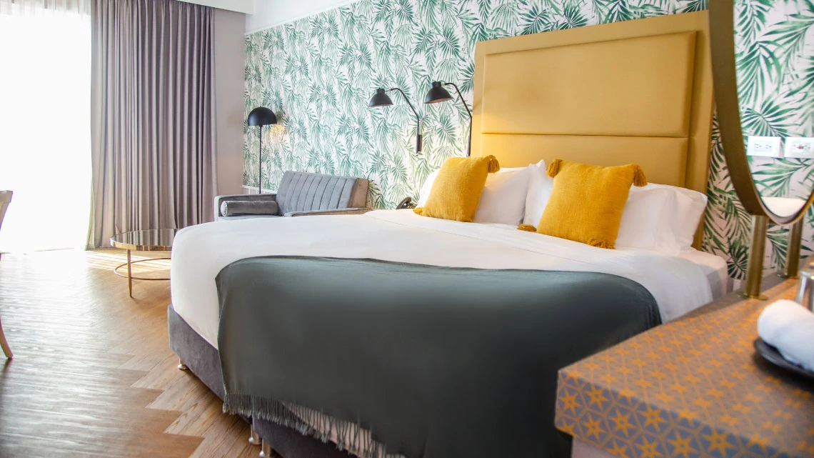Radisson Individuals® green, white, yellow linens on bed in hotel room with gray couch and colorful wallpaper
