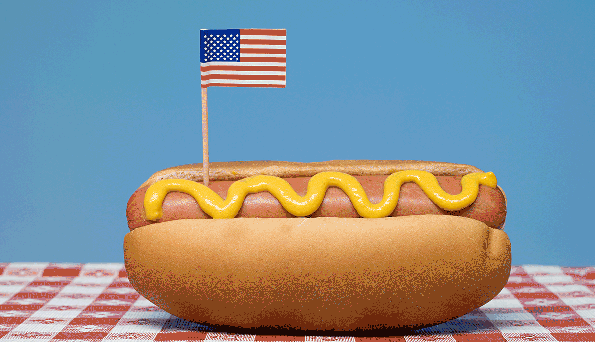 a photo and graphic illustration shows a hot dog on a picnic table with fireworks going off in the background