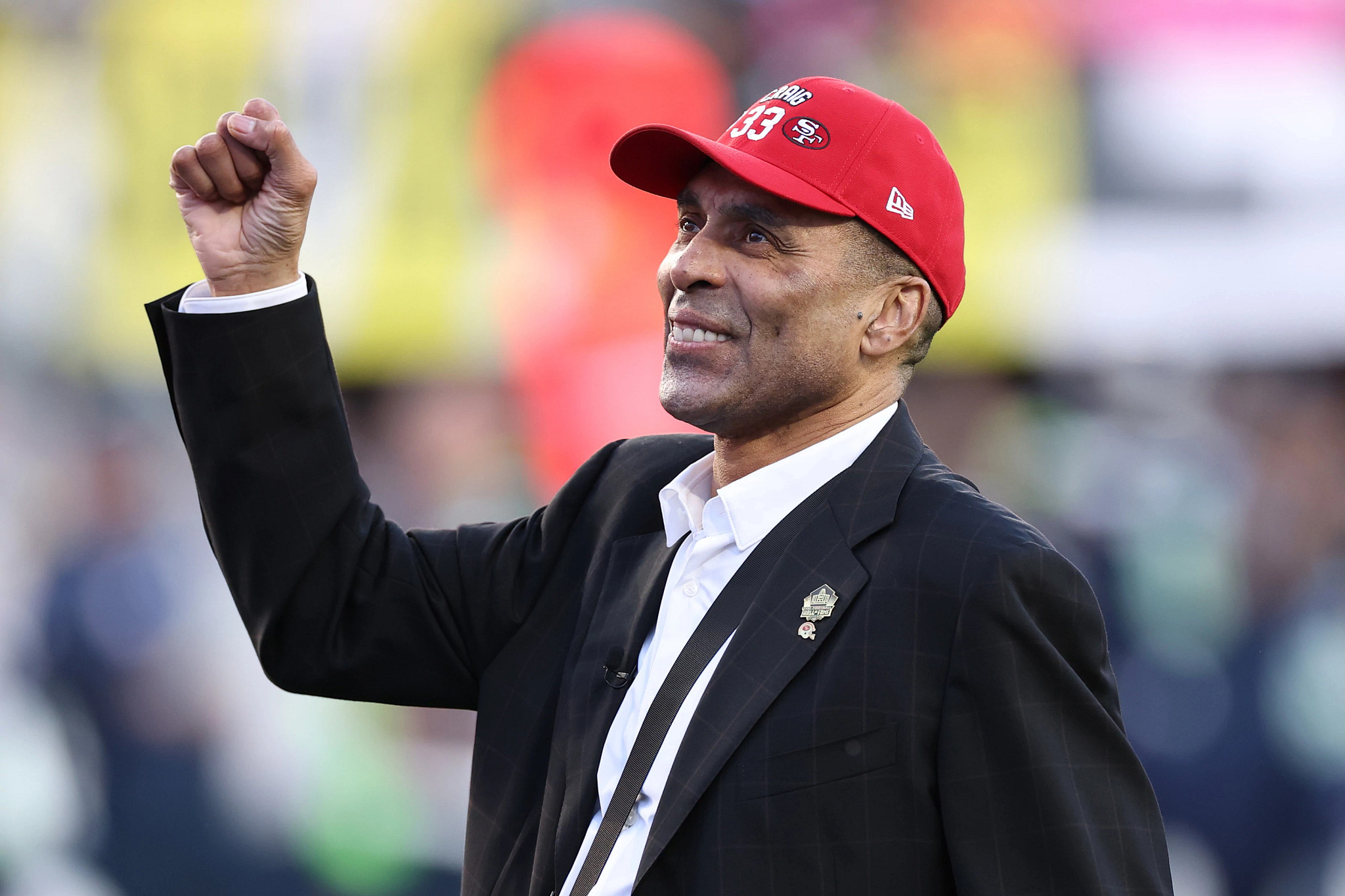 roger craig, wearing a forty-niners cap, raising his hand to recognize fans