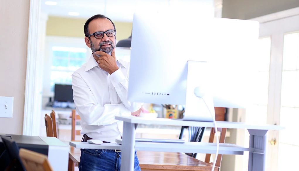 Standing is a great way to stave off the health hazards associated with sitting for long periods of time A man using a standing computer desk inside a home