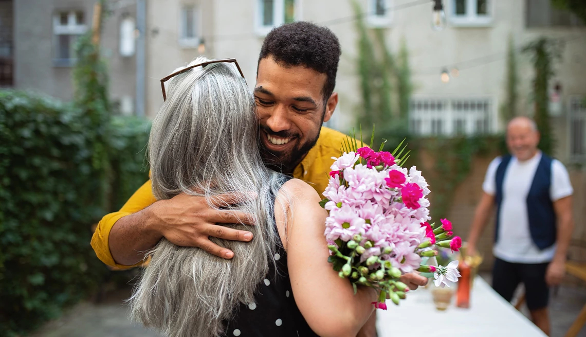 Man hugging his mother while holding bouquet of flowers