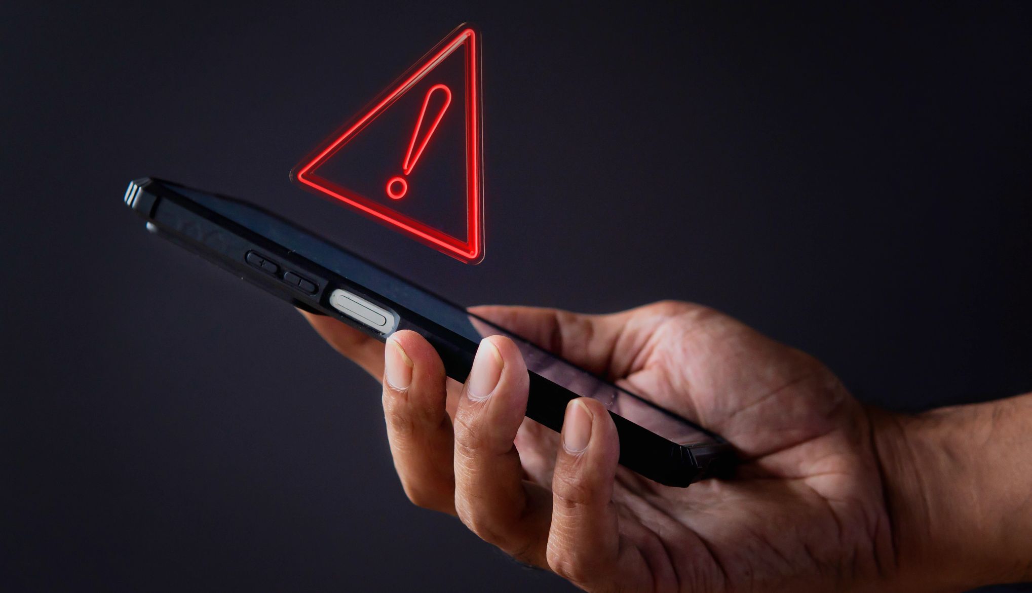 VSAFE se creó para ayudar a los veteranos víctimas de estafas Una mano sostiene un teléfono con un símbolo de advertencia encima.